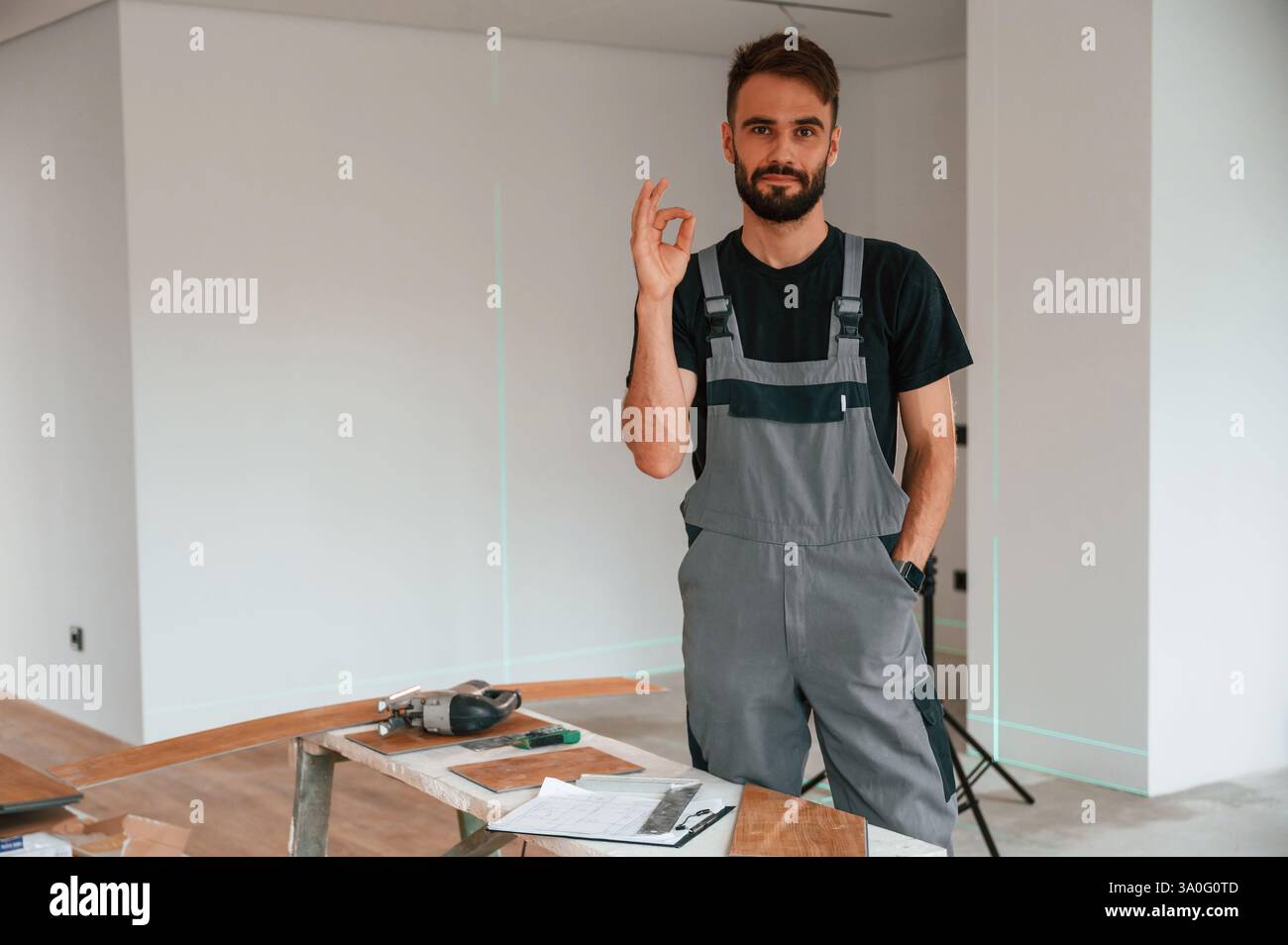 Stehend und zeigt eine gute Geste. Man installiert einen neuen laminierten Holzboden. Stockfoto