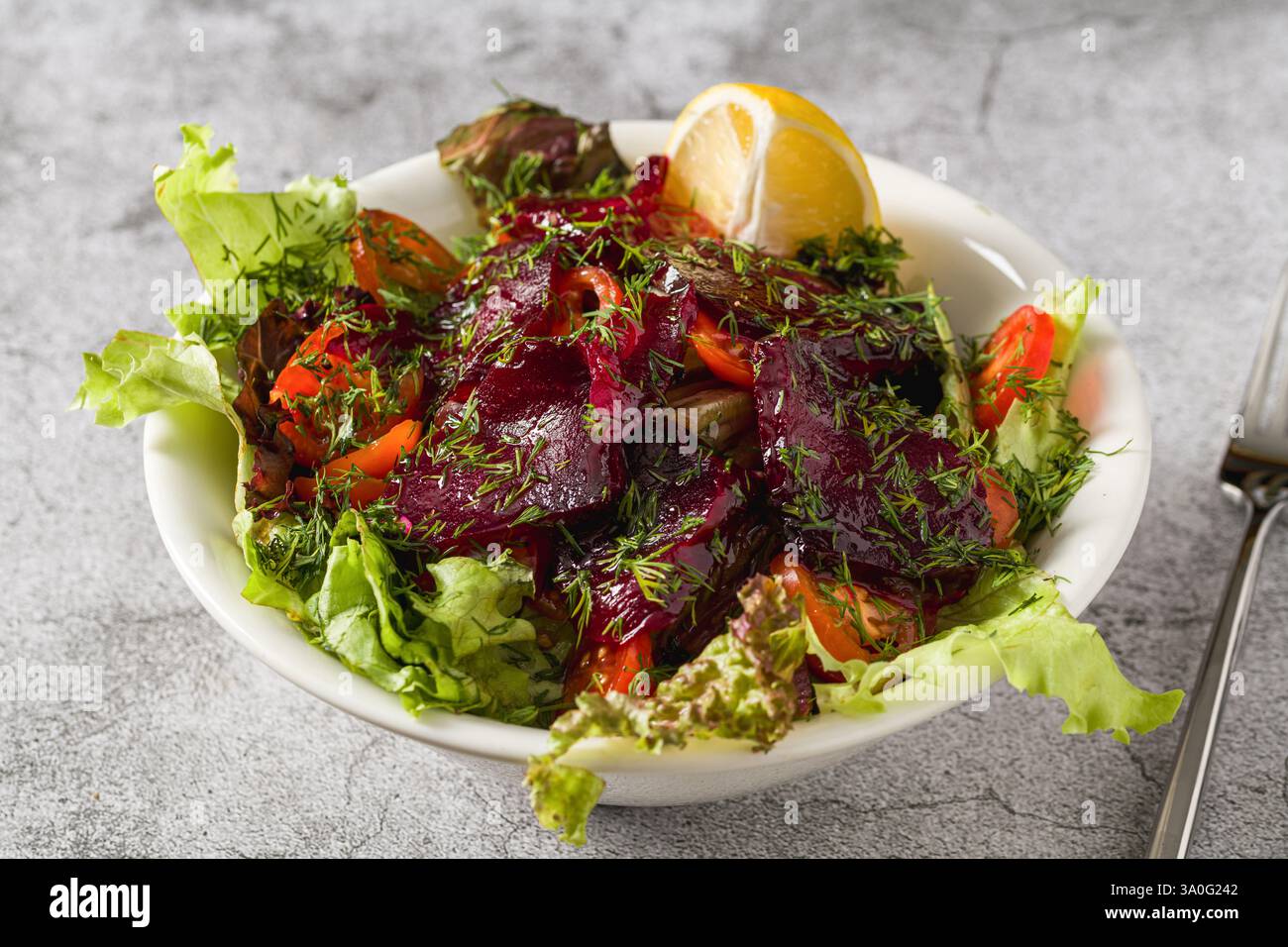 Rote-Bete-Salat mit Gemüse, Tomaten und Dill auf einem Steintisch Stockfoto