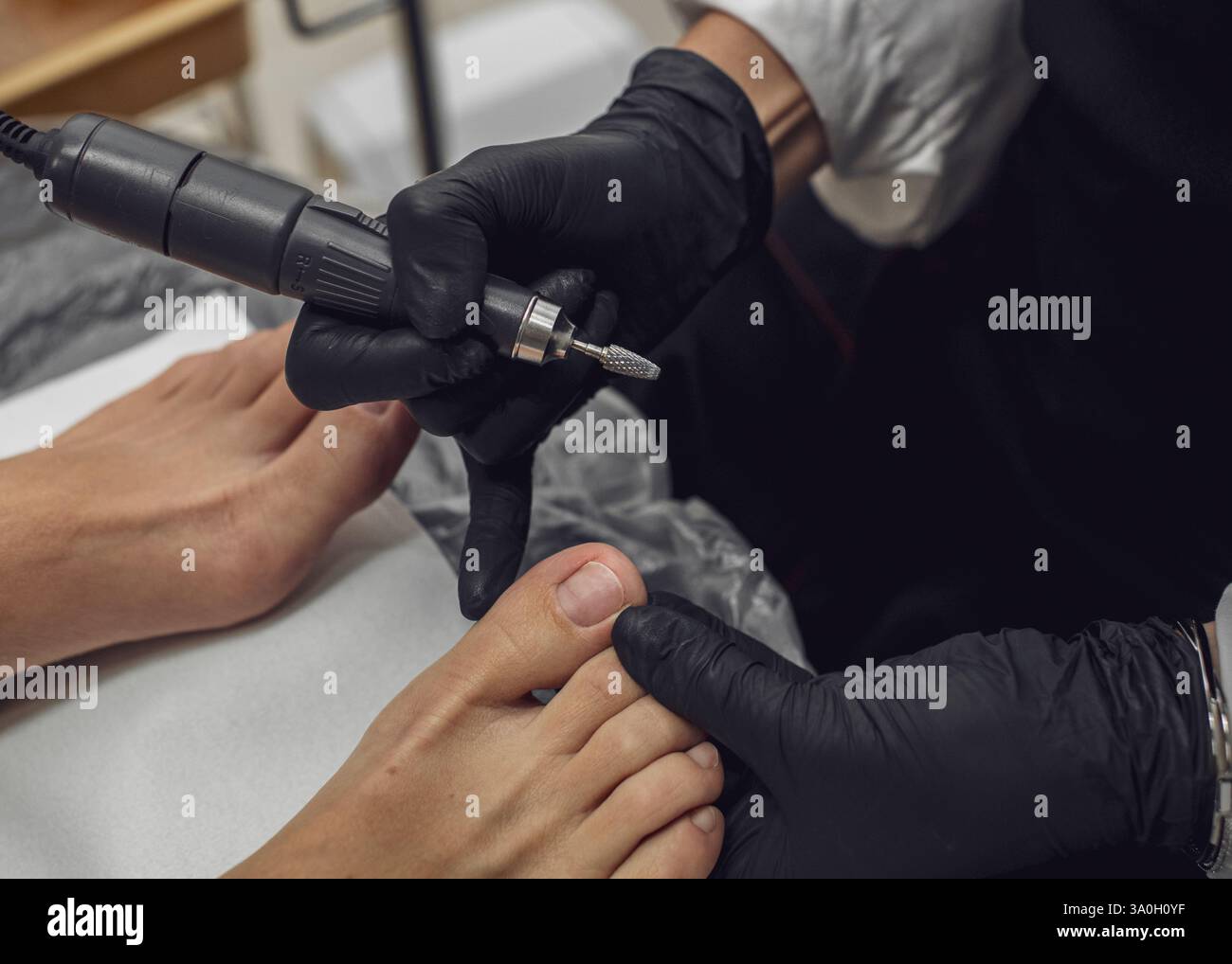 Der Meister führt eine Hardware-Pediküre in einem Schönheitssalon durch. Die Verarbeitung des Fußes mit Hilfe von professionellen Geräten und Schneidern. Stockfoto