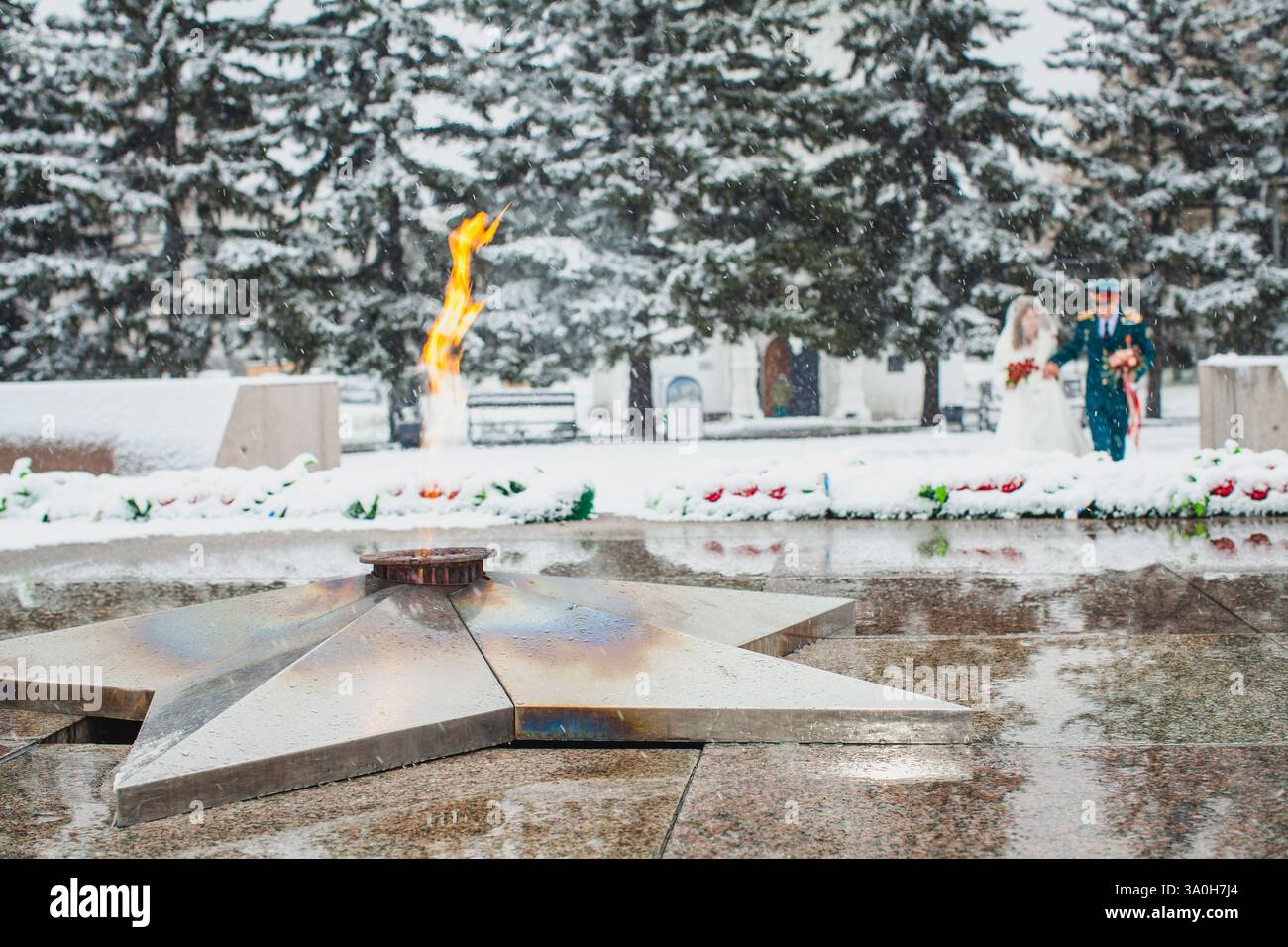 Ewige Flamme brennt auf einem Denkmal in einer verschneiten Umgebung mit einem verschwommenen Paar im Hintergrund Stockfoto