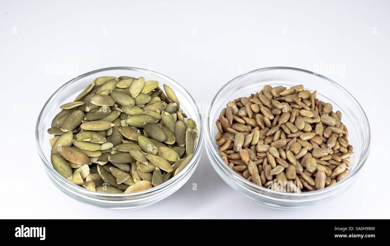 In zwei Glasschalen werden grüne Kürbiskerne und braune Sonnenblumenkerne präsentiert, die nahrhafte Snacks hervorheben. Dieses Setup betont gesunde Ernährung Choi Stockfoto