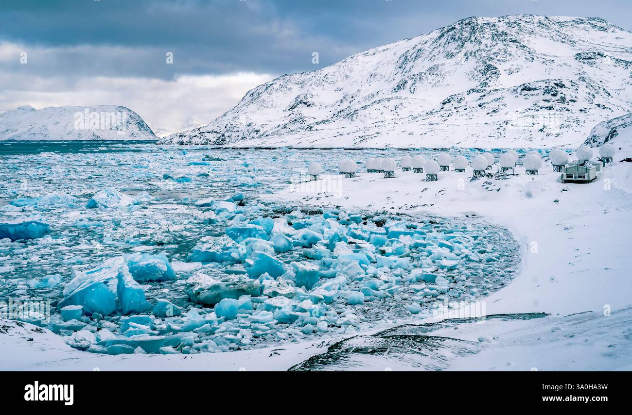 Eine atemberaubende Winterlandschaft mit einem gefrorenen Meer mit großen Eisbergen, die über das Wasser verstreut sind. Schneebedeckte Berge erheben sich im Hintergrund darunter Stockfoto