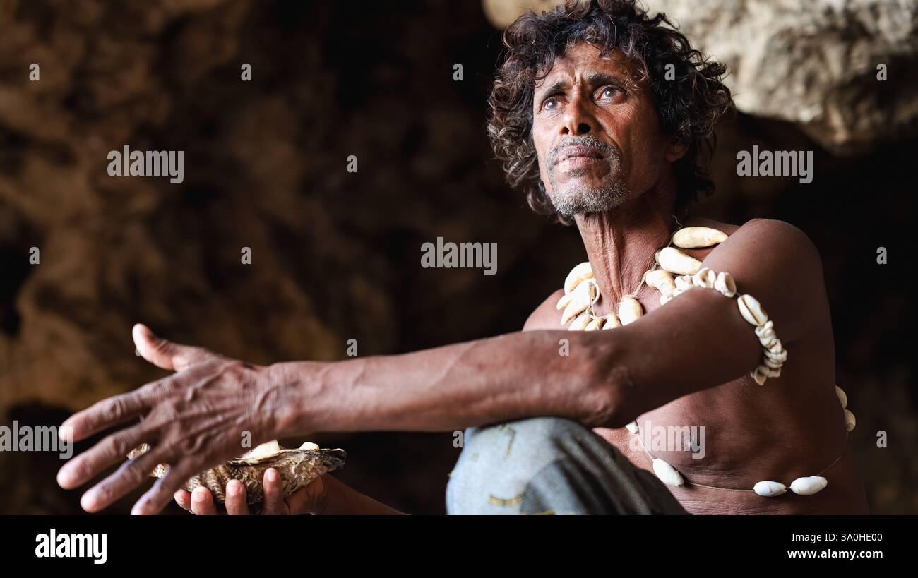 Ein Mann aus Socotra sitzt in einer Höhle, die mit Muschelschmuck geschmückt ist und traditionelle kulturelle Aktivitäten mit kontemplativem Ausdruck ausübt. Stockfoto