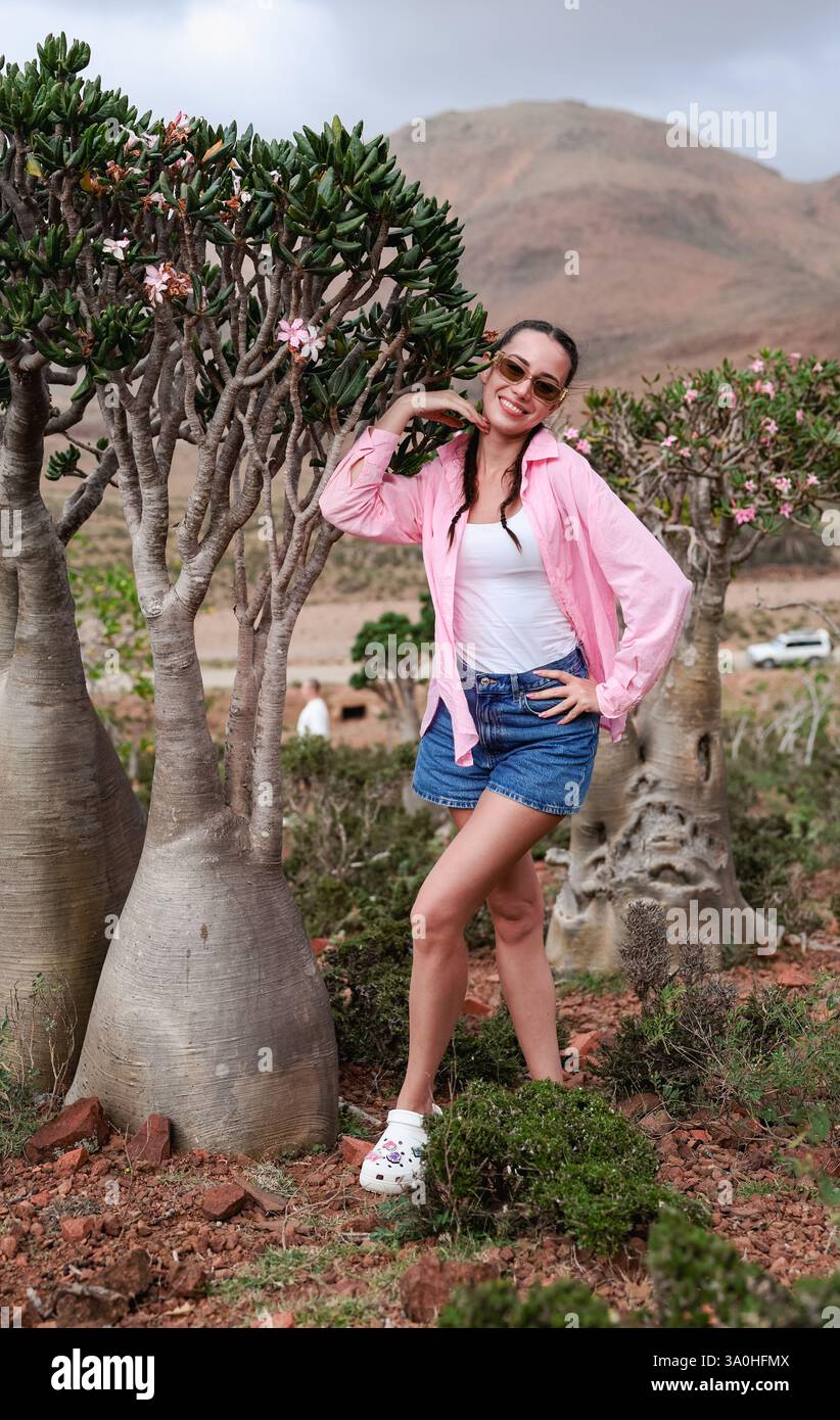 Ein Tourist posiert fröhlich zwischen den markanten Bäumen von Socotra und genießt die einzigartige Schönheit dieser abgelegenen Insellandschaft. Stockfoto