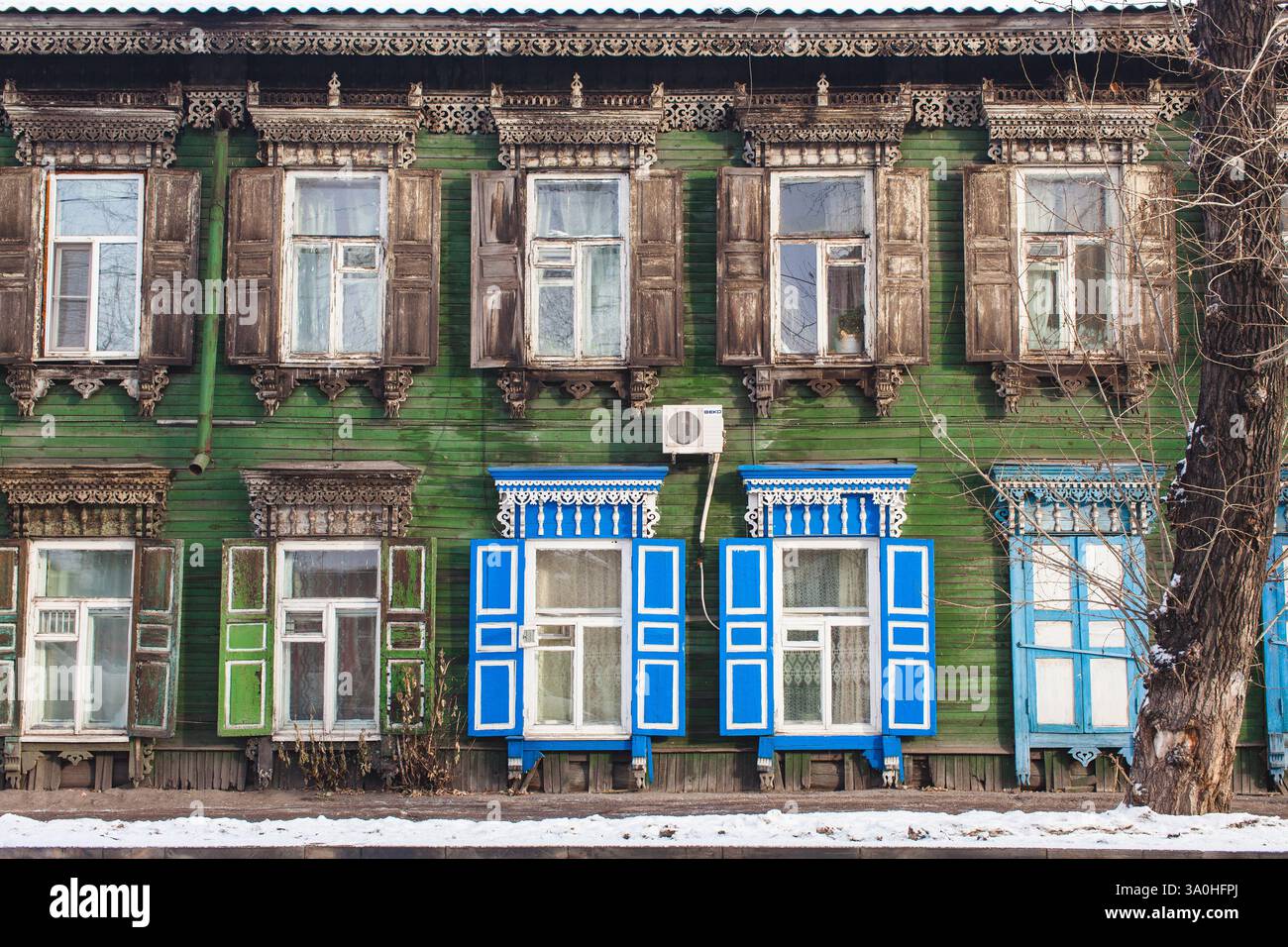 Ein historisches Holzhaus mit grünem Äußeren, mit aufwendig geschnitzten Fensterrahmen und Fensterläden. Die obere Reihe ist mit verwittertem, dunkelbraunem Sch versehen Stockfoto