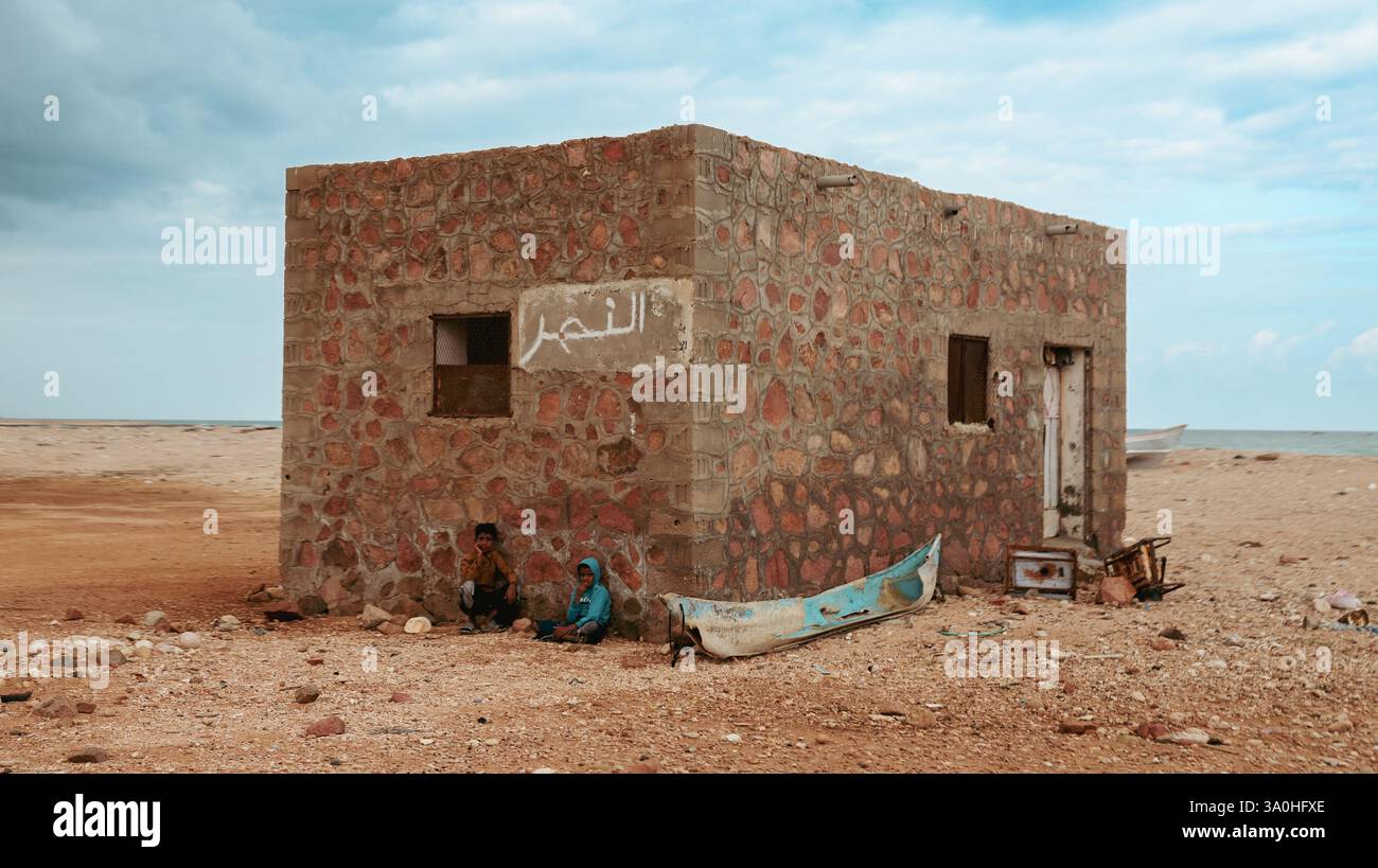 Zwei Personen finden Unterkunft neben einem Steingebäude an der Küste von Socotra, umgeben von natürlicher Schönheit. Stockfoto