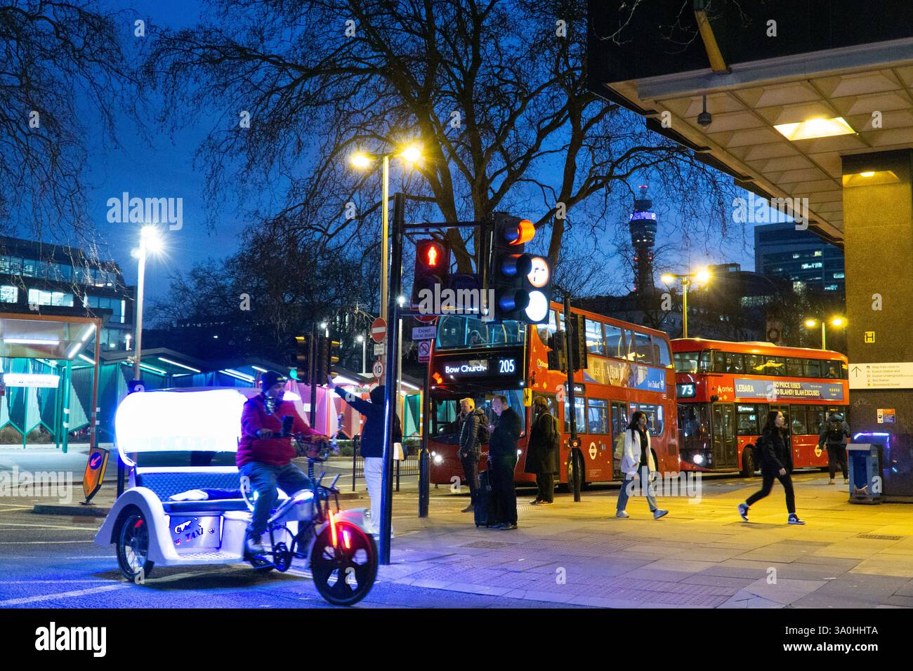 London, UK, 3. März 2025: Vor dem Bahnhof Euston bringen die klassischen roten Londoner Doppeldeckerbusse die Personenbusse auf ihre Reise und der Telecom Tower hebt sich vor dem Abenddämmerhimmel hervor. Ein leeres Pedi-Cab fährt in der Seitenstraße vorbei. Anna Watson/Alamy Stockfoto