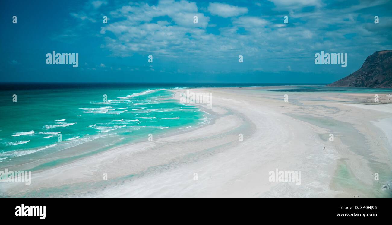 Die atemberaubende Küste von Socotra bietet unberührten Sand und leuchtende türkisfarbene Wellen unter einem hellblauen Himmel, was eine ruhige Atmosphäre schafft. Stockfoto