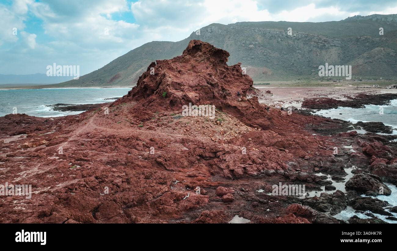 Besucher bestaunen die markanten roten Felsformationen und die atemberaubende Aussicht auf die Küste von Socotra Island bei Tageslicht. Stockfoto