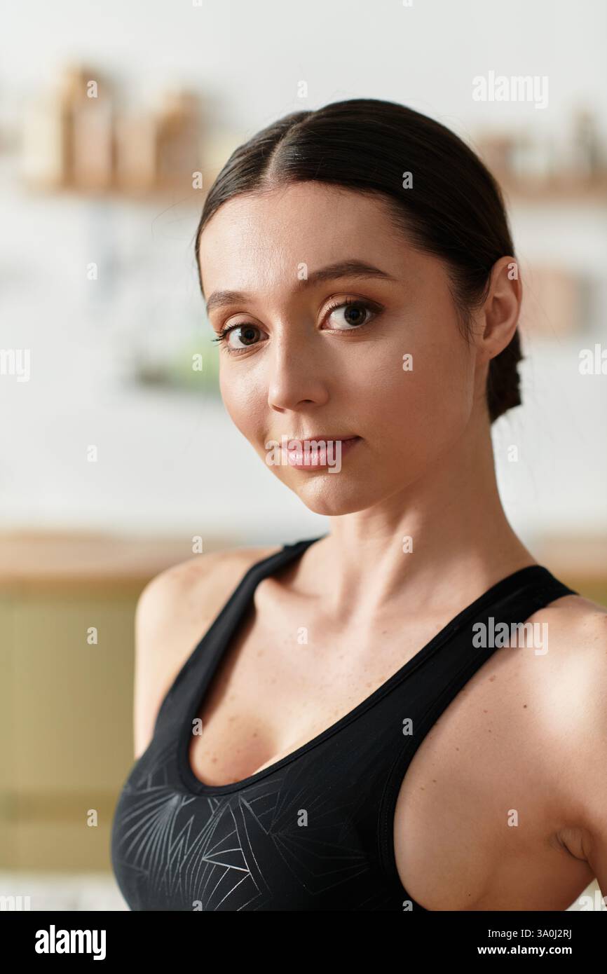 Schöne junge Frau in schwarzer Sportbekleidung aktiv in ihrer modernen Wohnung. Stockfoto