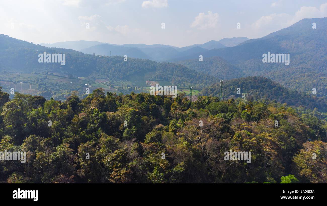 Aus der Vogelperspektive auf einen wunderschönen tropischen Wald, der die Bergkette im Norden Thailands bedeckt, an einem sonnigen Tag mit trübem, staubigen Himmel Stockfoto