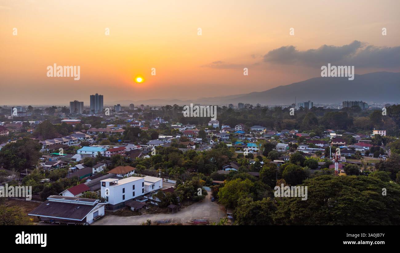 Luftaufnahme von Wohnhäusern, Gebäuden und Bäumen in Chiang Mai, Thailand, während eines farbenfrohen Sonnenuntergangs mit dem Berg Doi Suthep im Hintergrund wi Stockfoto