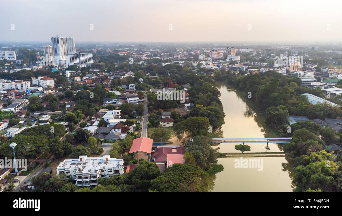 Luftaufnahme von Wohnhäusern, Gebäuden, grünen Bäumen und dem Fluss Ping, der während des Sonnenuntergangs mit verschmutzter Luft durch die Stadt Chiang Mai in Thailand fließt Stockfoto