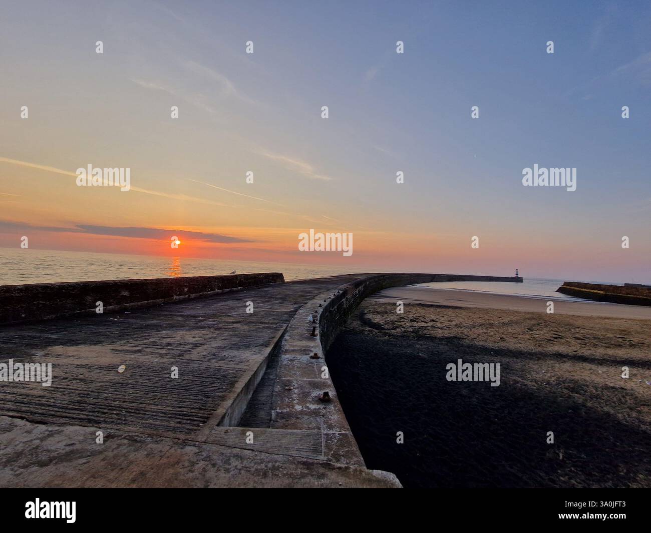 Goldener Sonnenaufgang über Seaham Beach an einem warmen Sommermorgen, der ein ruhiges Leuchten über die ruhigen Wellen wirft. - Smartphone-aufgenommenes Stockfoto