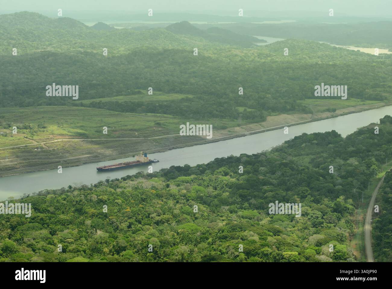 Ein Blick aus der Vogelperspektive auf den Panamakanal, umgeben von üppigem Grün, mit einem großen Schiff, das in den Kanal einfährt. Die Szene zeigt das technische Wunderwerk von Th Stockfoto