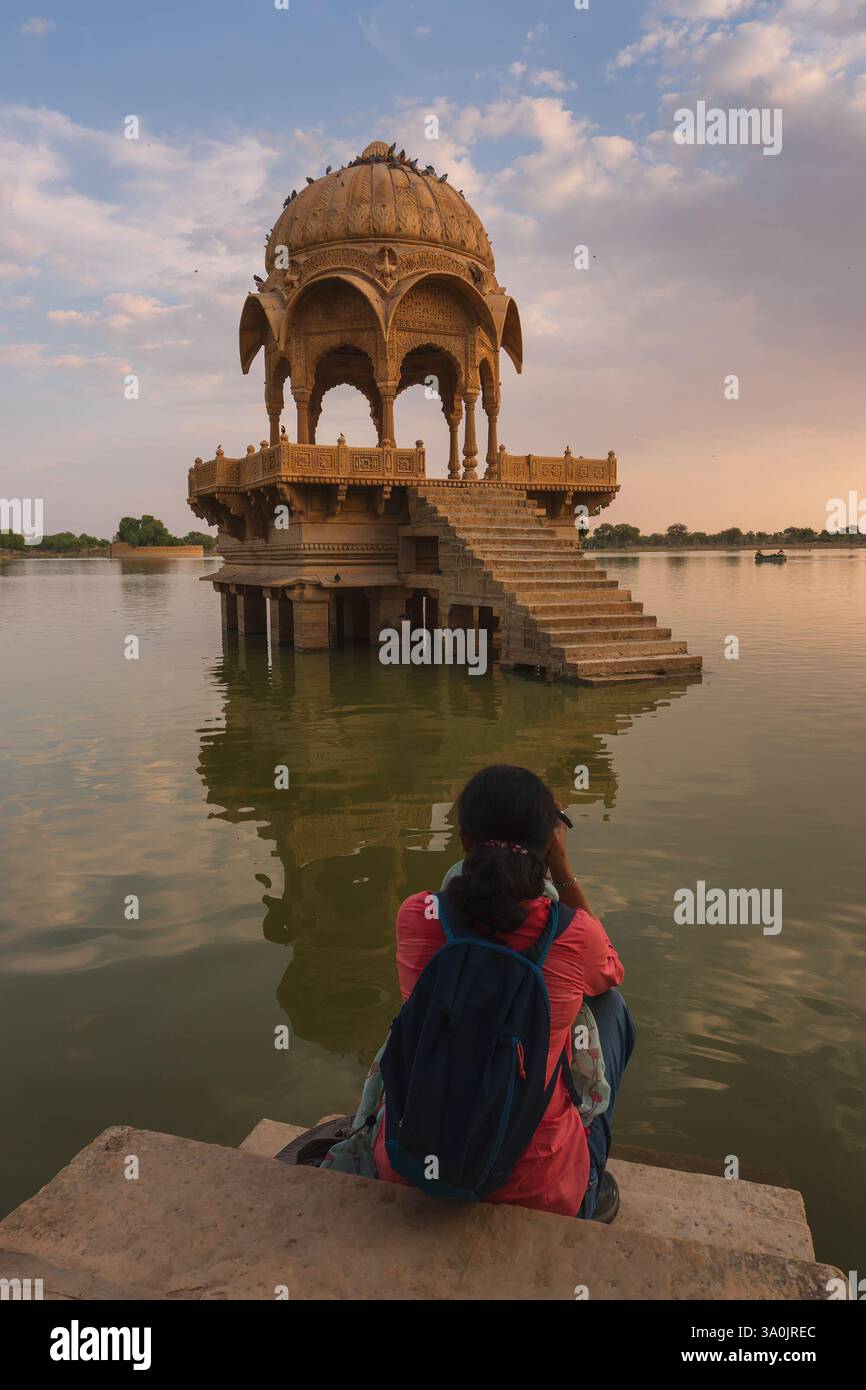 Indische Reisende, Fotografin, die Chhatris und Schreine fotografiert und auf dem Wasser des Gadisar-Sees reflektiert. Sonnenuntergang. Stockfoto