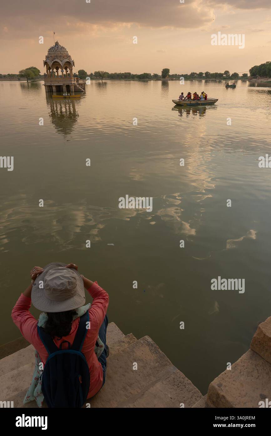 Indische Reisende, Fotografin, die Chhatris und Schreine fotografiert und auf dem Wasser des Gadisar-Sees reflektiert. Sonnenuntergang. Stockfoto