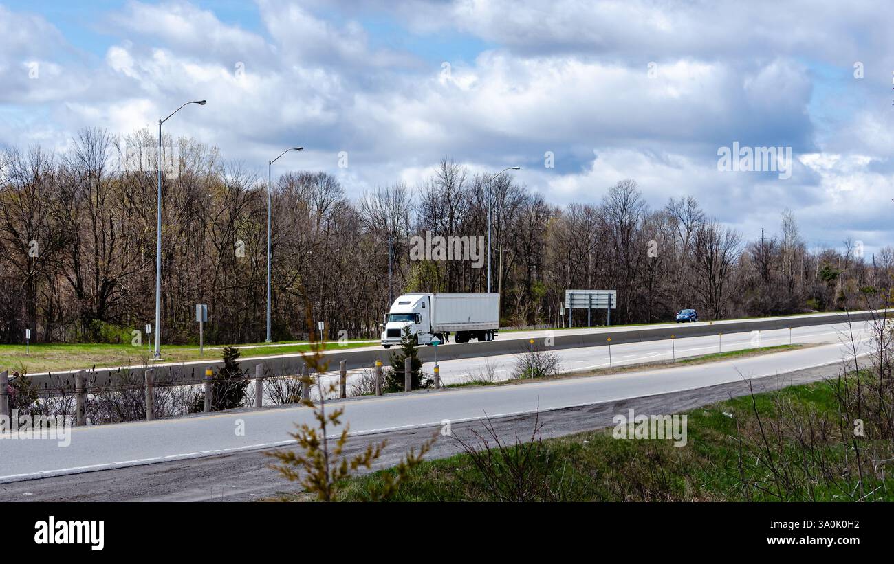 Einsamer Transportwagen und Auto auf einer Autobahn im Frühling unter bewölktem Himmel. Stockfoto