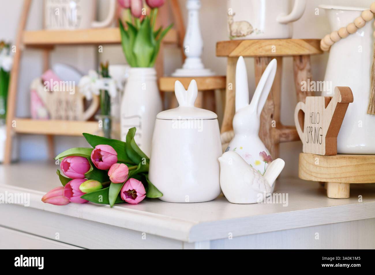 Süßes saisonales Osterdekor mit kleinem Kanister mit Hasenohren, Vogel- und pinkfarbenem Tulpenblumenboquet Stockfoto