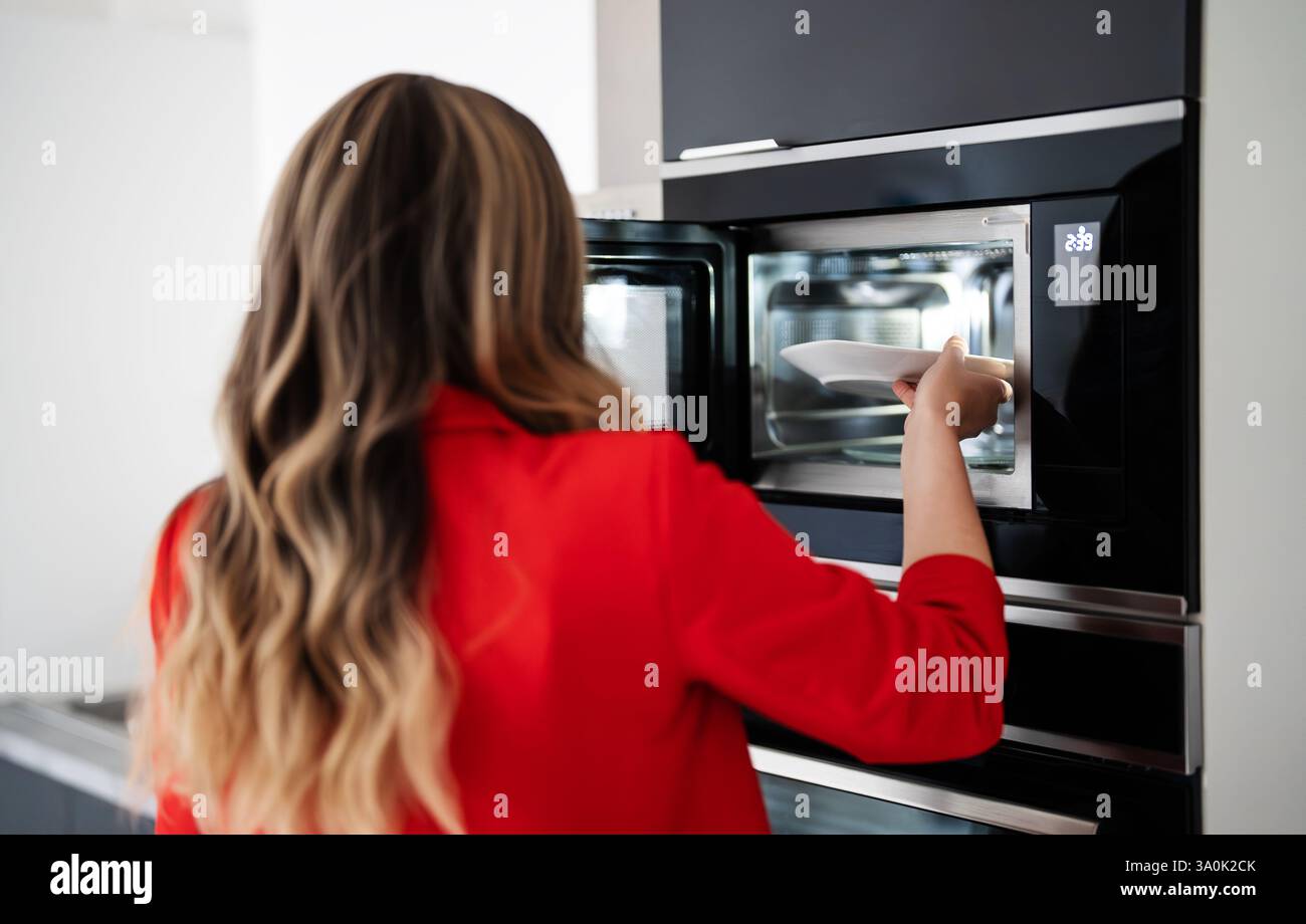 Frau, die einen Teller mit Essen in die Mikrowelle legt. Stockfoto