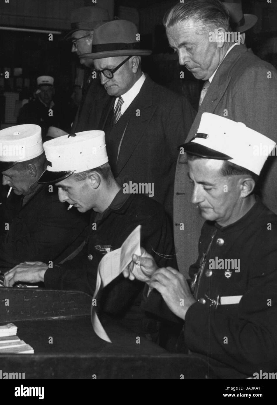 Industriegericht -- Präsident (Mr. Justice Barry), der die Arbeitsbedingungen im Straßenbahndepot in der Light Street überprüft, gestern um 6,40 Uhr. Hier, mit Tramways General Manager (Herr G.A. Preston, links) und Tramways Union Sekretär (Herr W. McCormack, rechts). Seine Ehre beobachtet Straßenbahnführer, die ihre Fahrkarten überprüfen. August 1954. Stockfoto