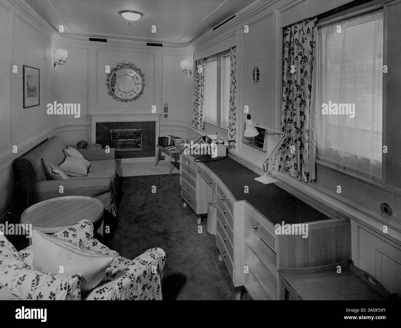 Royal Apartments An Bord Der 'Britannia'. -- das private Wohnzimmer der Königin, das einen geschäftsähnlichen, eingebauten Knielocher-Schreibtisch hat, an dem Ihre Majestät viel Arbeit verbrachte. Die glasierten Chintz-Vorhänge mit farbenfrohen Rosenknospen und Möbel aus weißer Esche verleihen diesem Zimmer jedoch einen charmanten femininen Touch. Das „Intercom“-System ist mit dem privaten Zimmer des Duke of Edinburgh verbunden. Mai 1954. (Foto von Fox Photos). Stockfoto