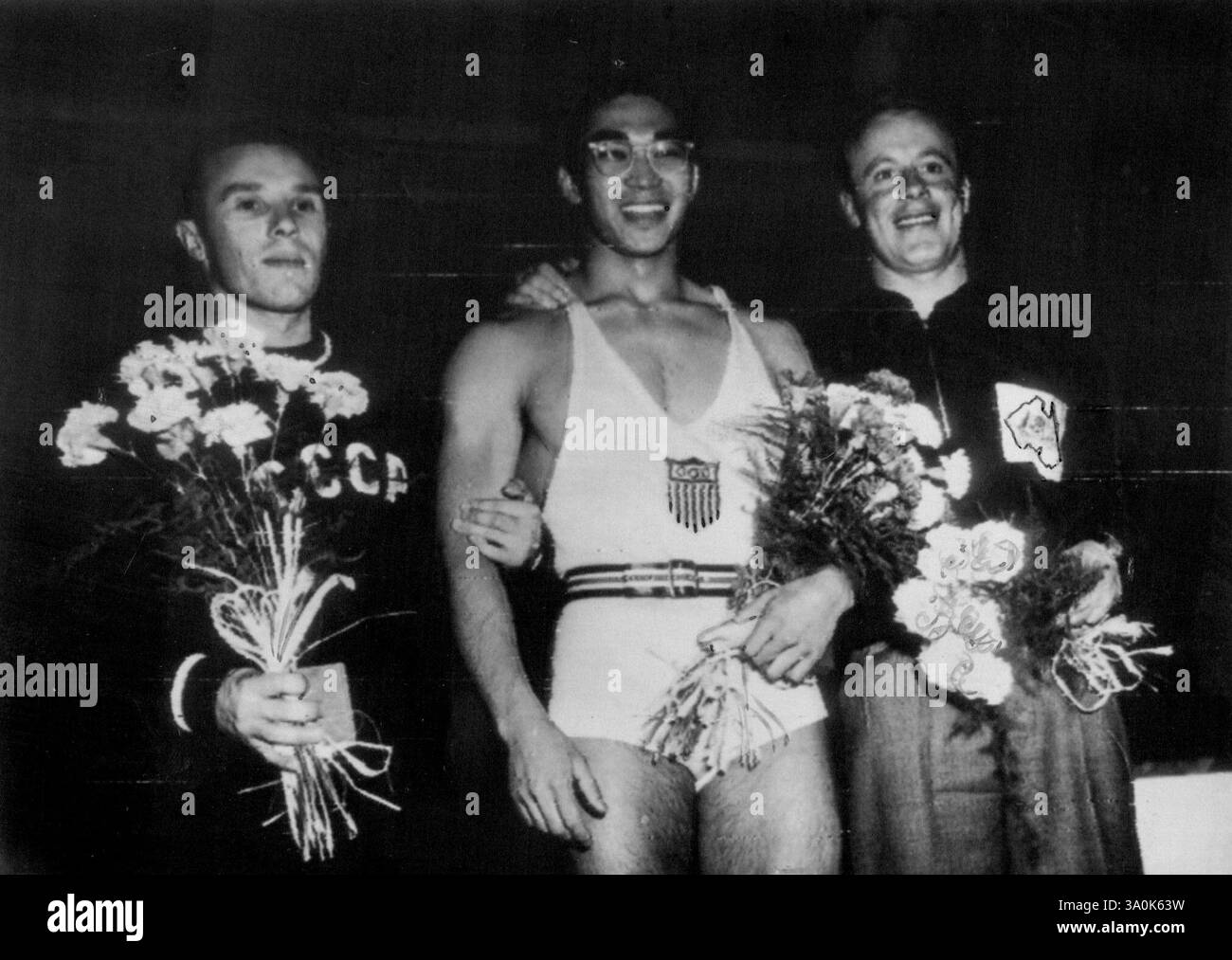 Gewichtheber in Helsinki in der Leichtgewichtsklasse werden von Blumen verzaubert. Der US-Amerikaner T. Kono (Mitte) gewann den Russen E. Lopatin (links) und den Australier V. Barberis (rechts). Juli 1952. (Foto von Radio Picture). Stockfoto