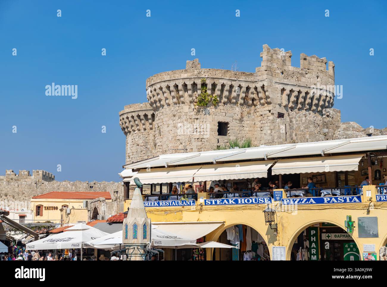 Ein Bild des Hippokrates-Platzes in Rhodos City, mit dem Sea Gate, das die nahe gelegenen Restaurants überragt. Stockfoto