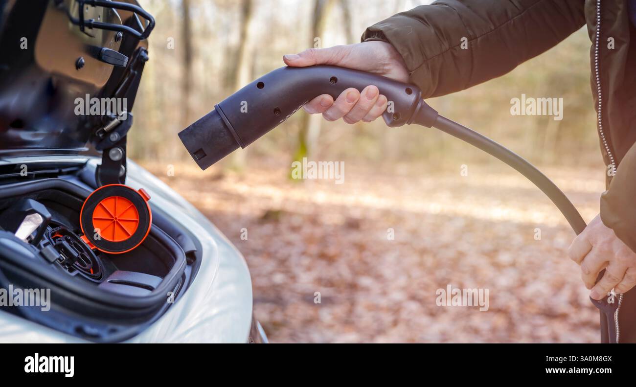 Nahaufnahme des Ladeanschlusses eines Elektroautos mit einer Hand, die einen Ladeanschluss einsteckt. Stockfoto