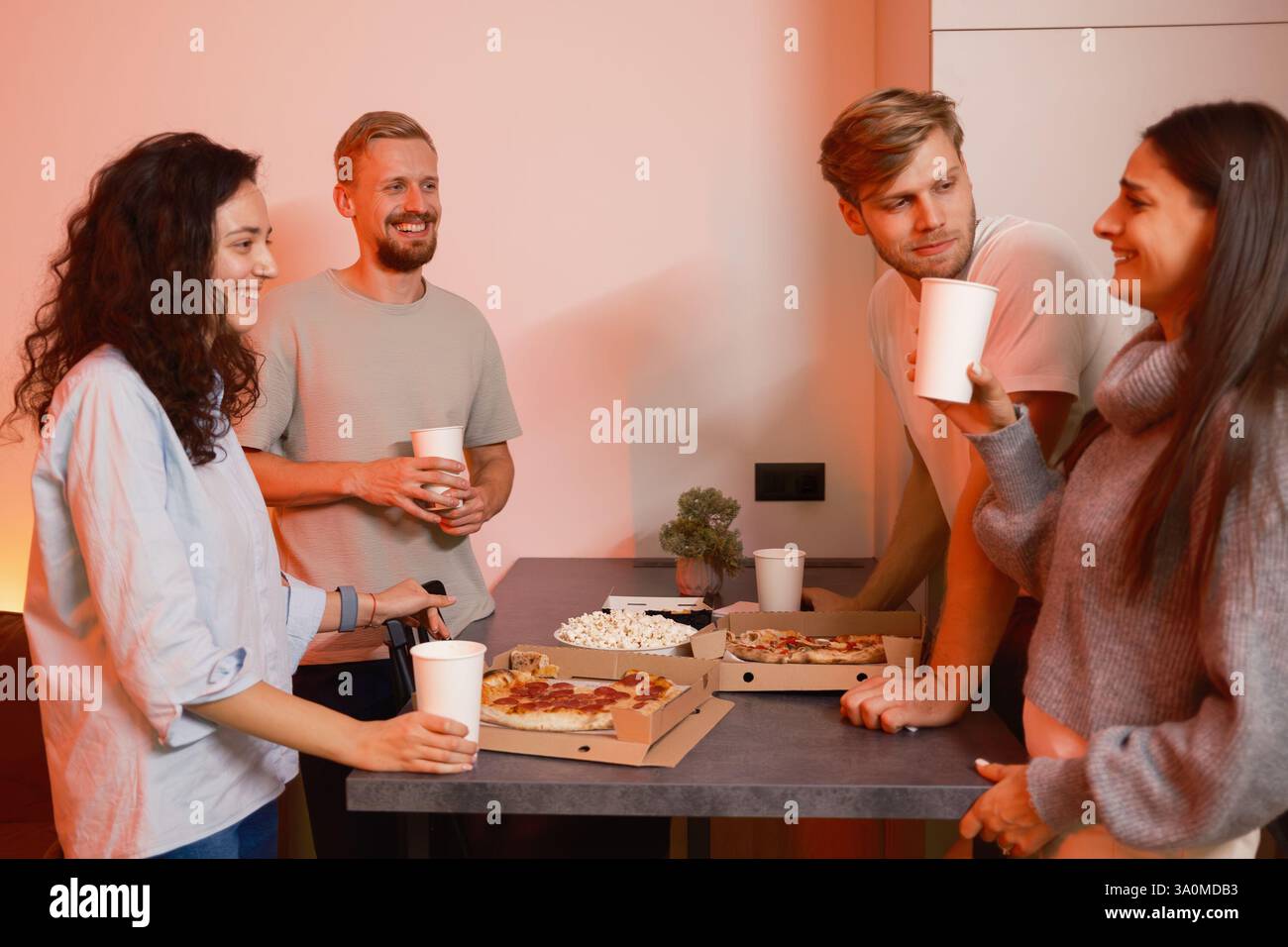 Eine Gruppe von Freunden genießt gemeinsam Pizza und Getränke bei einem gemütlichen Treffen zu Hause Stockfoto