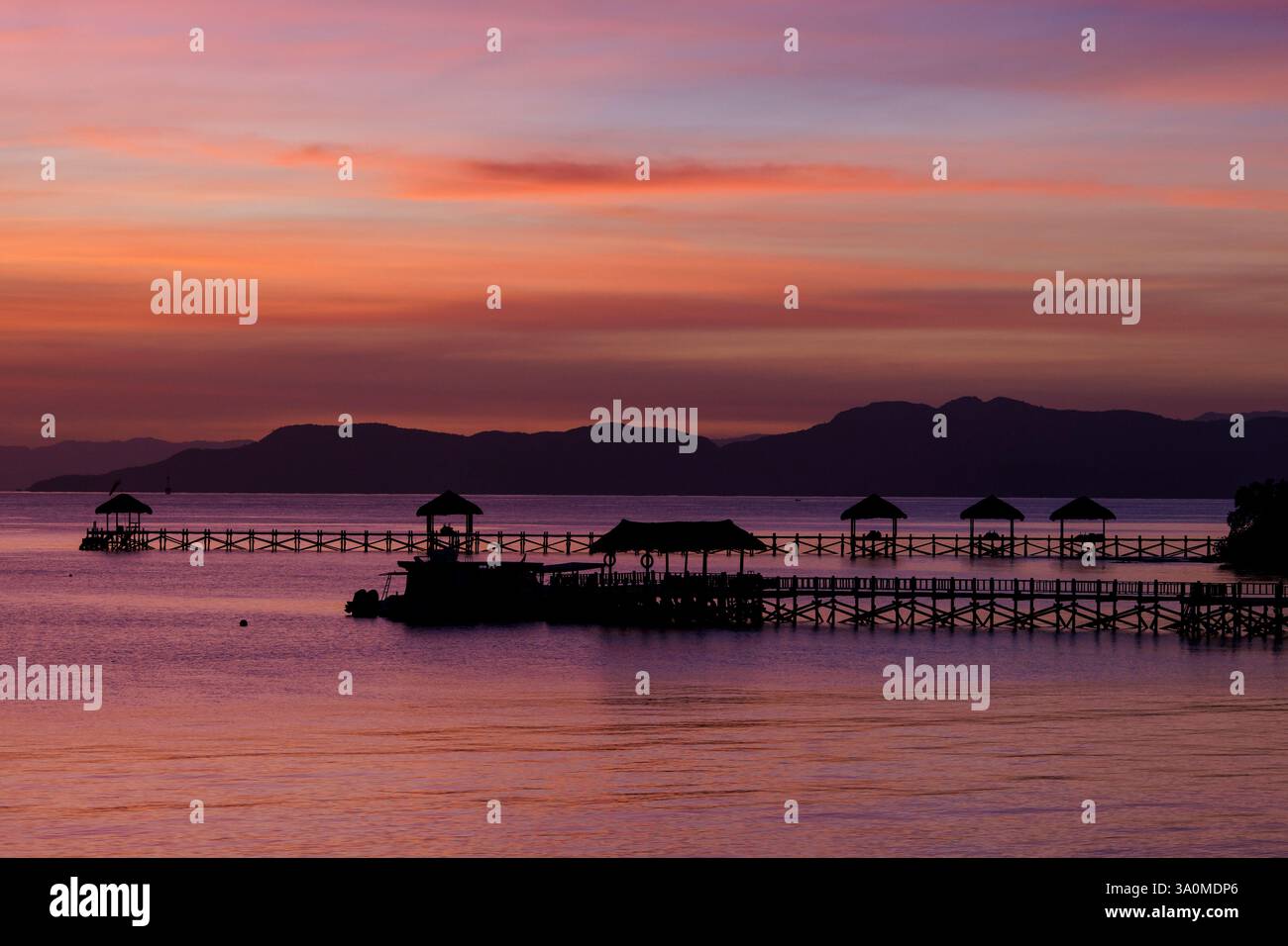 Blick auf den Sonnenaufgang auf die Docks und Tiki-Hütten auf der Insel Seraja Kecil, auch bekannt als Seraya, vor der Küste von Labuan Bajo, Komodo-Inseln, Indonesien. Stockfoto