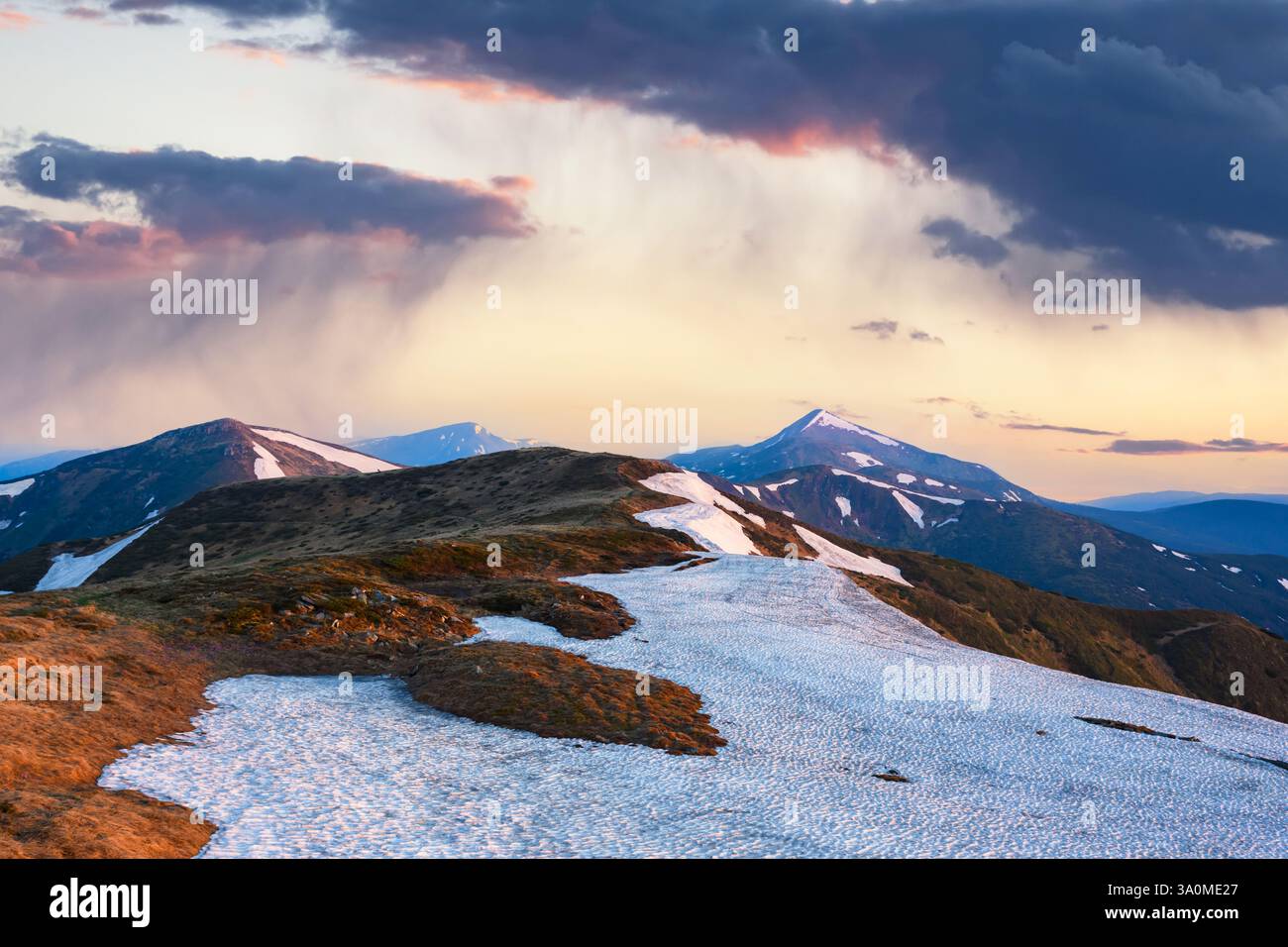 Frühlingsregen in den hohen Bergen. Schneebedeckte Hügel und hohe Gipfel, die von der untergehenden Sonne erstrahlen. Landschaftsfotografie Stockfoto