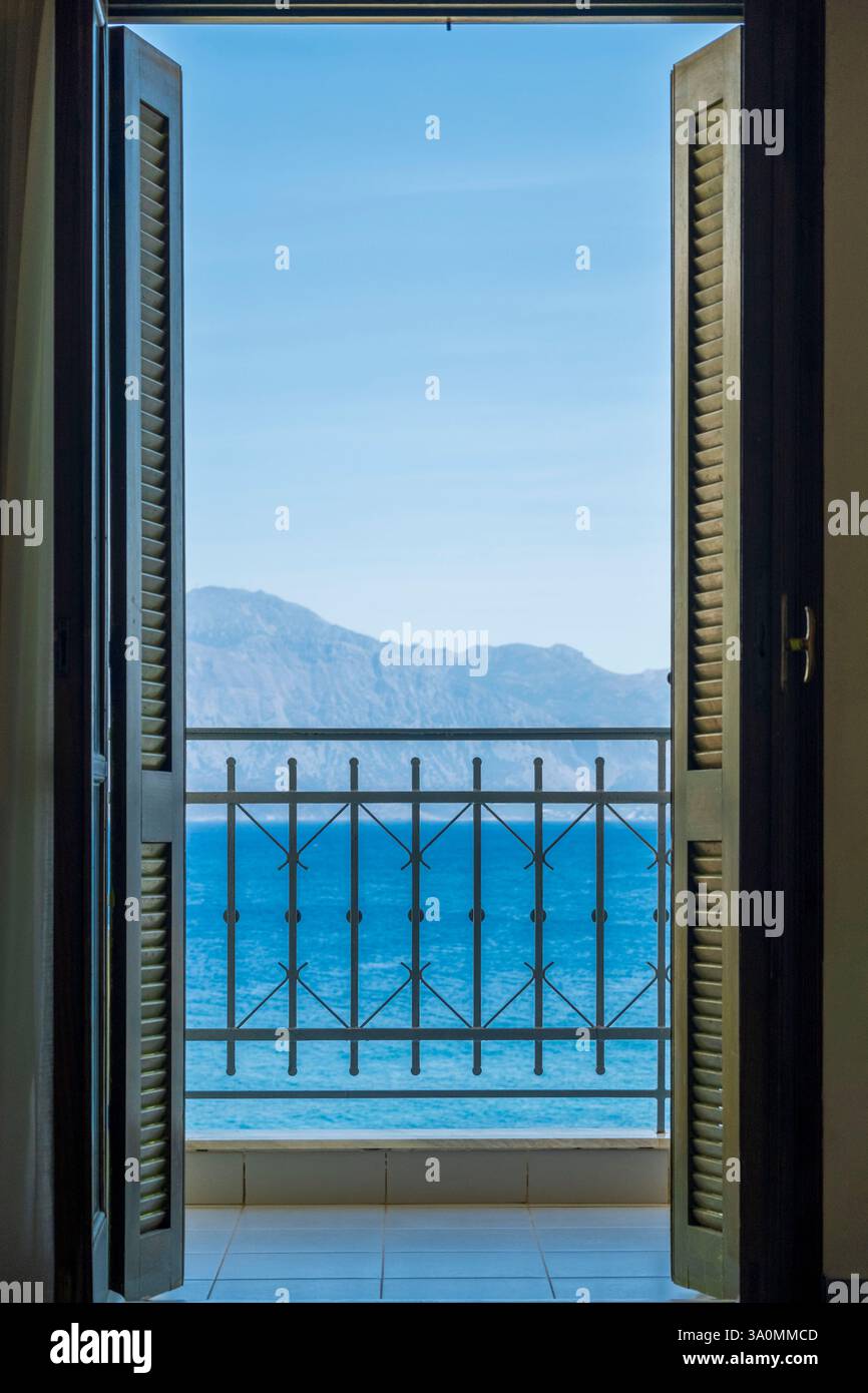 Mediterrane Terrasse mit Meerblick, Holzladen und schmiedeeisernem Zaun im späten Morgenlicht. Ruhige mediterrane Terrasse mit Blick auf das Hotel Stockfoto