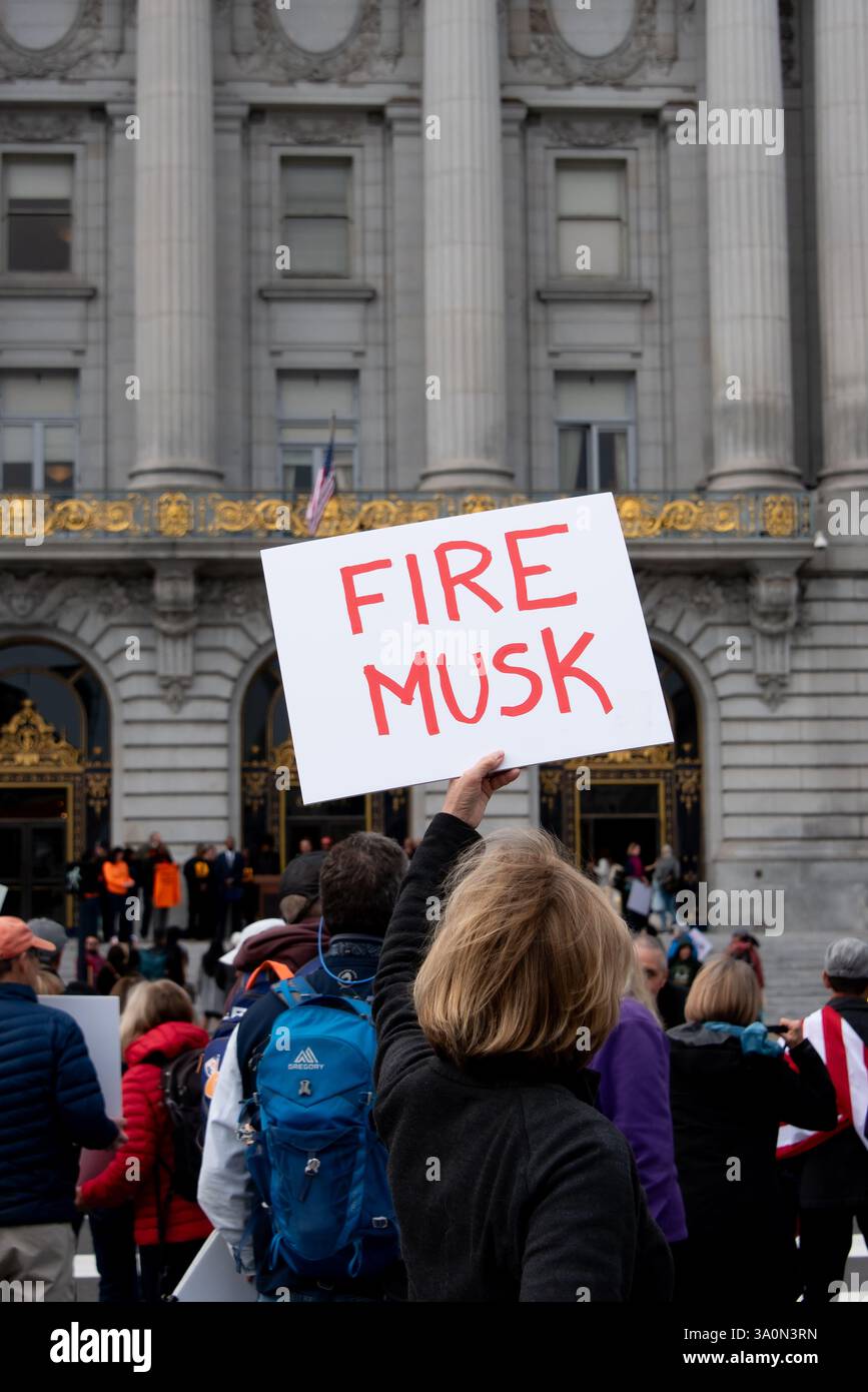San Francisco, USA. März 2025. Eine Frau hält ein Schild mit der Aufschrift „FIRE MUSK“, während sich Demonstranten vor dem Rathaus von San Francisco versammeln, um gegen Trumps Befehle und die Aktionen des DOGENTEAMS von Elon Musk zu protestieren. Quelle: Shelly Rivoli/Alamy Live News Stockfoto