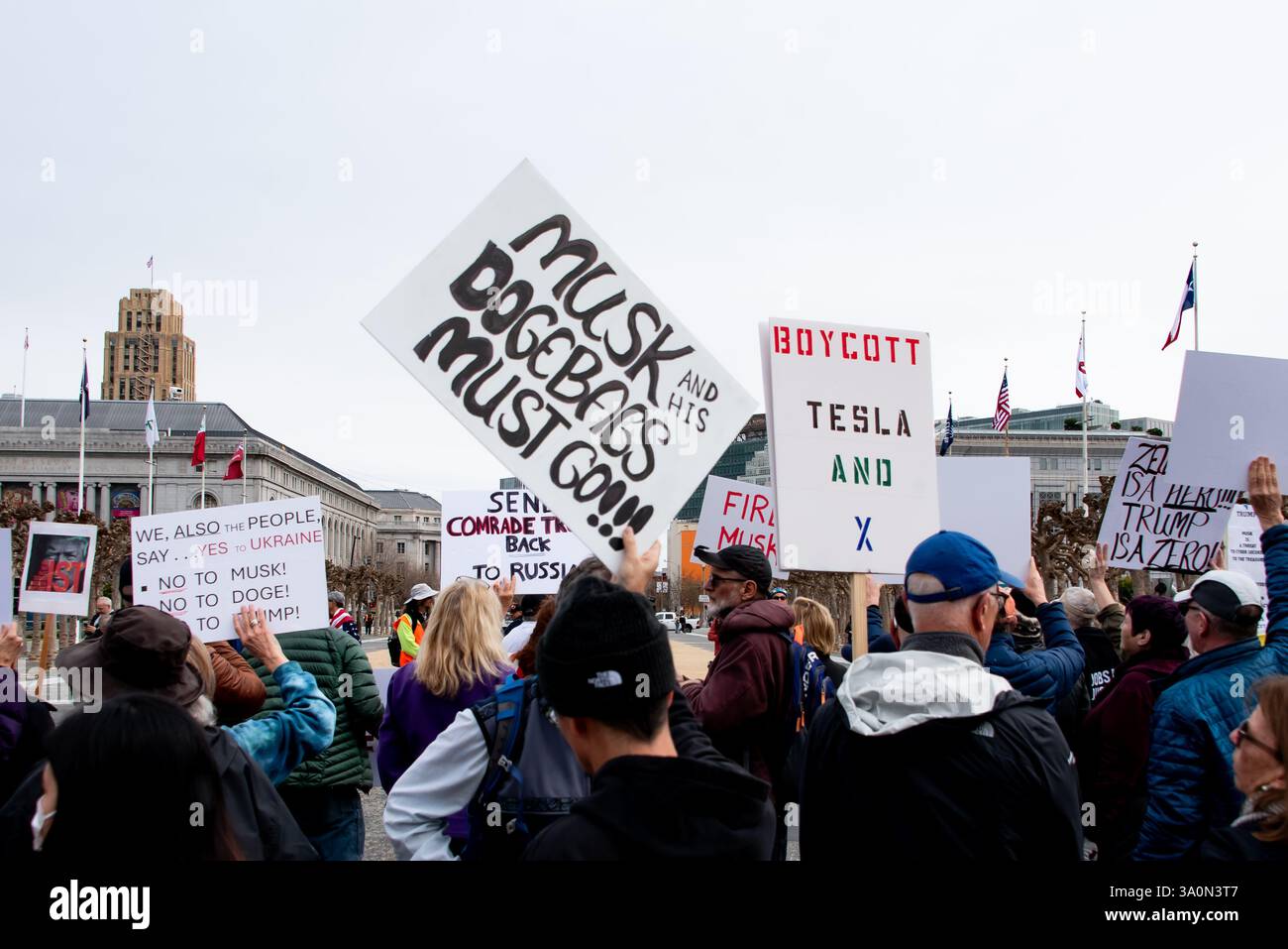 San Francisco, USA. März 2025. Demonstranten versammeln sich am Civic Center Plaza vor dem Rathaus von San Francisco, um gegen die Befehle von Präsident Trump und die Aktionen von Elon Musk und seinem DOGENTEAM zu protestieren. Auf den Schildern über der Menge stand: „Wir, auch das Volk, sagen ... Ja zur Ukraine, nein zu Moschus, nein zu DOGE,“ „Musk und seine Dogebags müssen gehen“ und „Boykott Tesla und X.“ Credit: Shelly Rivoli/Alamy Live News Stockfoto