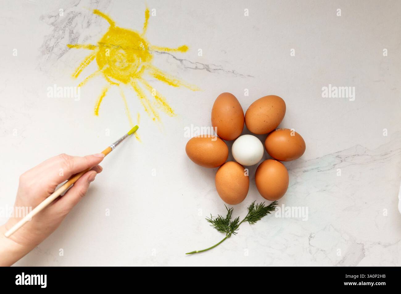 Eine geschickte Hand malt fachmännisch die strahlende Sonne mit wunderschönen bunten Eiern, die eine helle Blume auf glattem Marmor bilden, eine Osterdekoration Stockfoto
