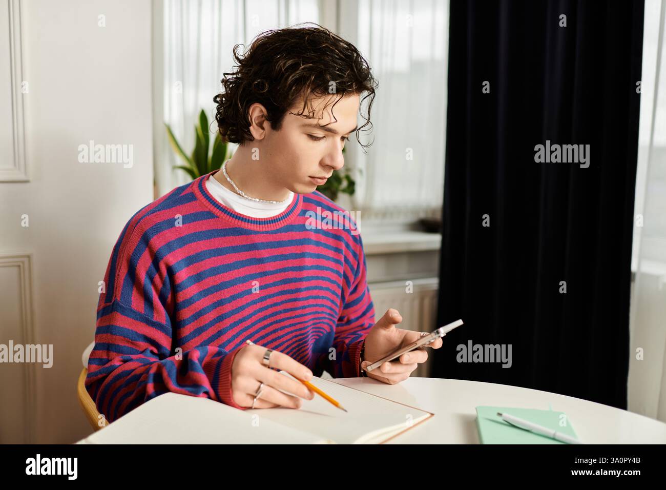 In einem eleganten Apartment konzentriert sich eine junge, nicht binäre Person mit lockigen Haaren auf ein Notebook. Stockfoto