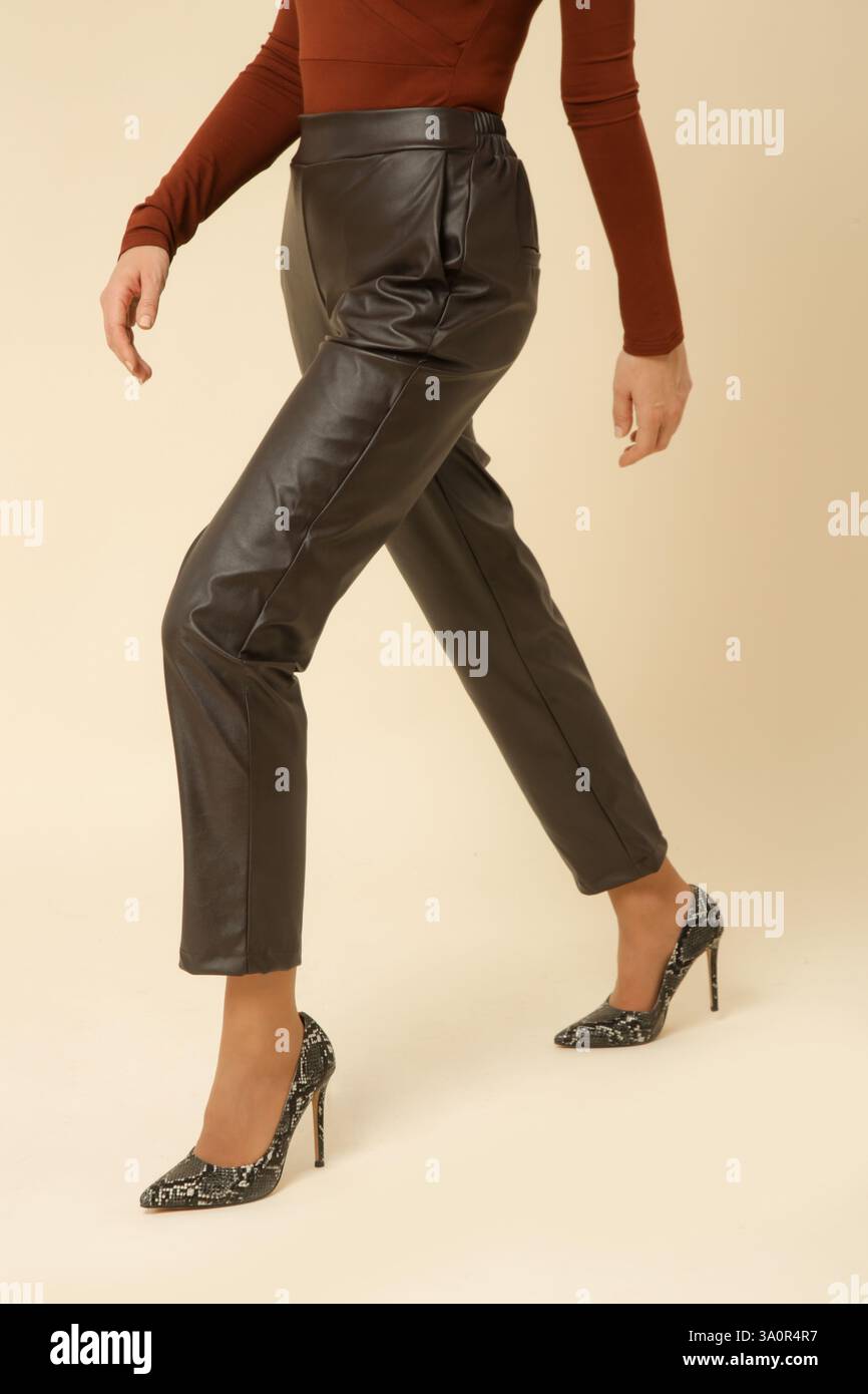 Studio-Fotografie eines jungen weiblichen Models in braunen Kunstlederhosen mit High Heels Stockfoto