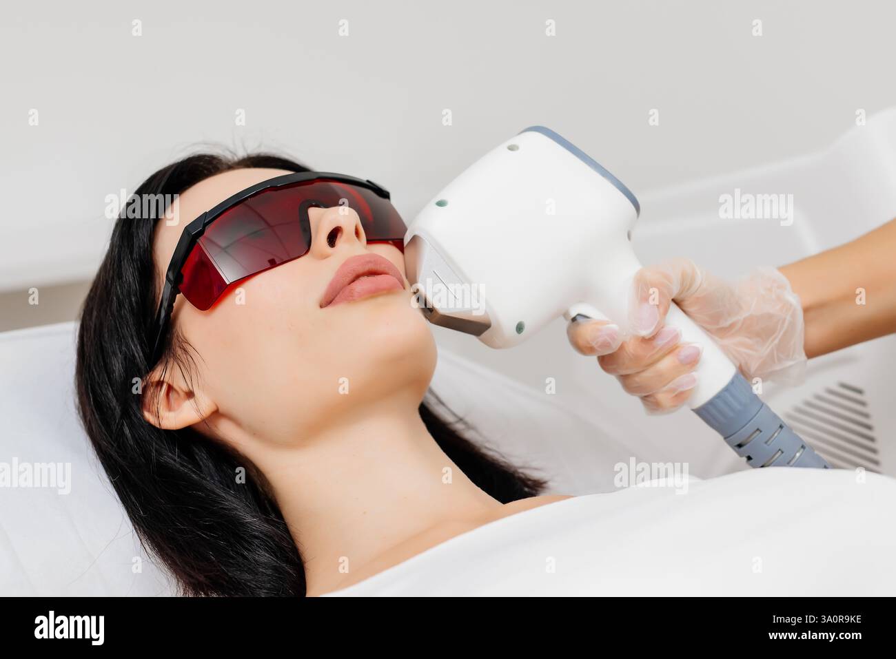 Die Therapeutin/Kosmetikerin führt eine Laserbehandlung auf dem Gesicht einer Frau in einer Schönheitsklinik durch. Nahaufnahme. Das Konzept der Werbung gesund Stockfoto Die Therapeutin/Kosmetikerin führt eine Laserbehandlung auf dem Gesicht einer Frau in einer Schönheitsklinik durch. Nahaufnahme. Das Konzept der Werbung gesund Stockfoto