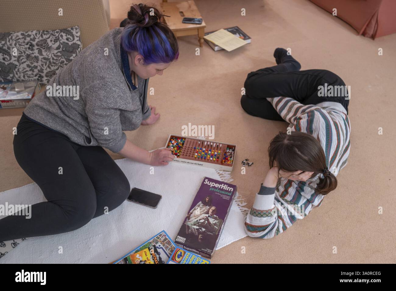 Zwei junge Frau, die ein Gesellschaftsspiel auf dem Teppich im Wohnzimmer spielt, Bayern, Deutschland, Europa Stockfoto