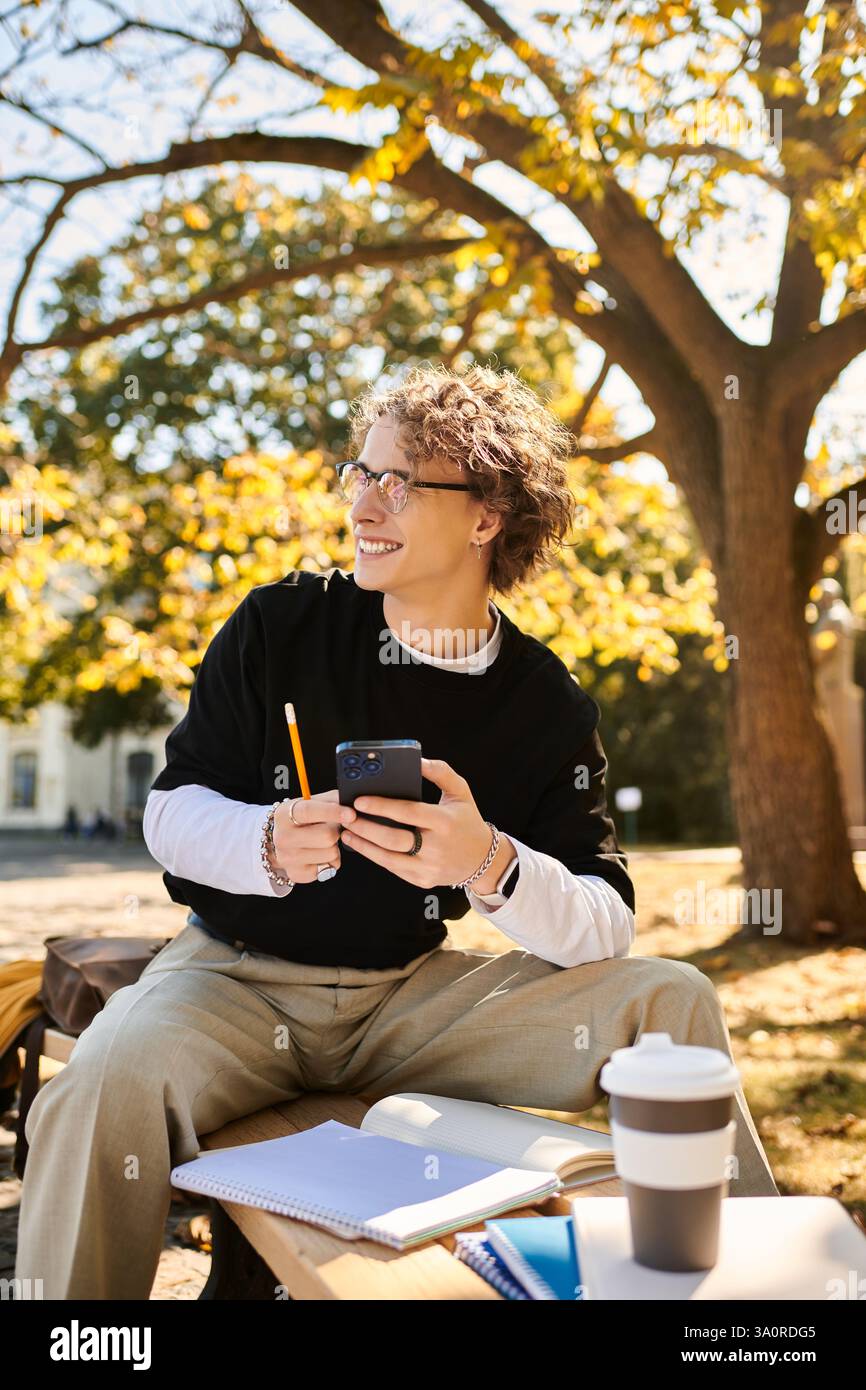 Ein stilvoller junger Mann studiert an einem Tisch mit seinem Smartphone bei hellem Sonnenlicht. Stockfoto