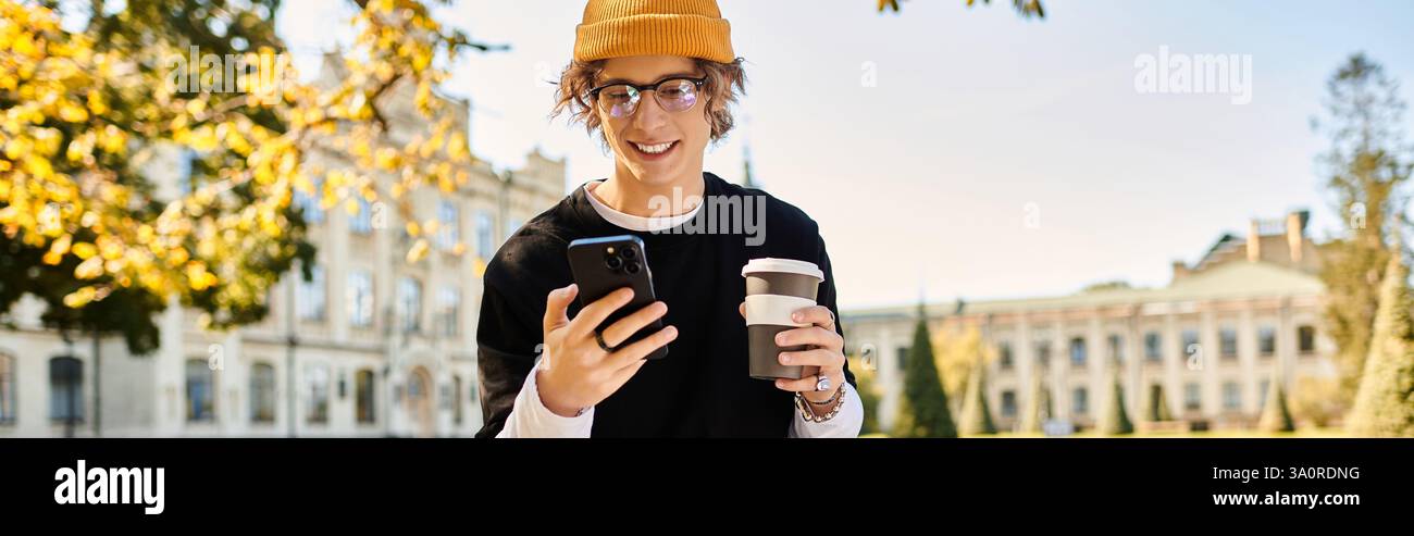 Ein Mann in einer Mütze und einer Brille lächelt auf sein Handy, während er Kaffee auf dem Campus genießt. Stockfoto