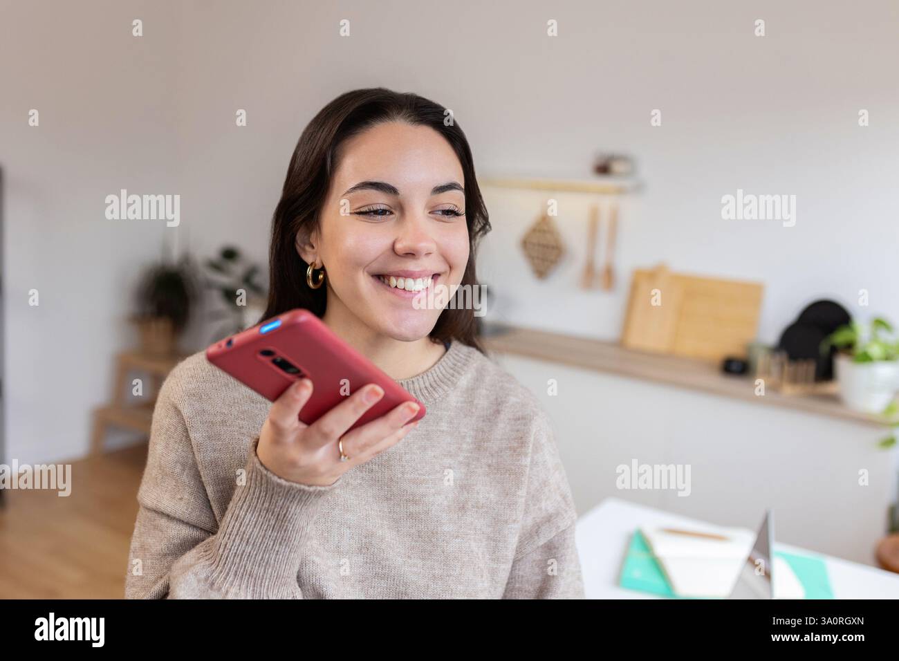 Junge glückliche Frau, die zu Hause Sprachnachrichten auf dem Smartphone aufnimmt Stockfoto