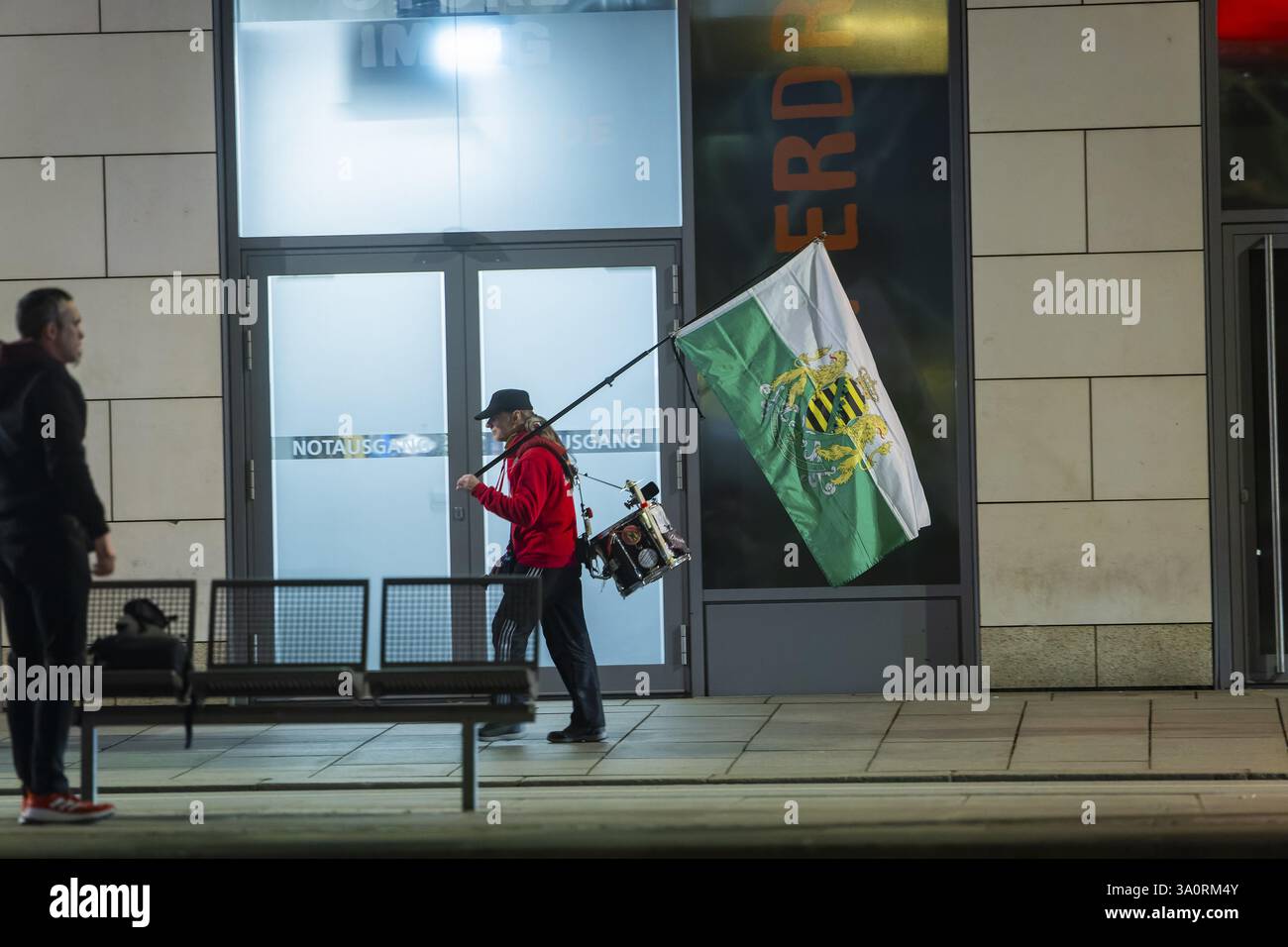Ein Passant sieht einen Unterstützer der radikalen Freisachsen an, der mit sächsischer Flagge und Trommel auf der Wilsdruffer Straße für die montags-Demonstration läuft Stockfoto