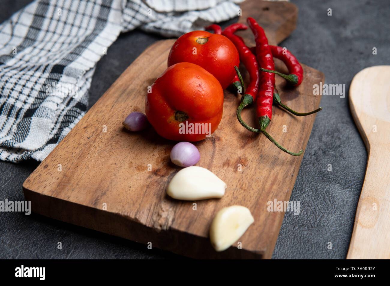 Ein hölzernes Schneidebrett mit frischen Zutaten, darunter reife rote Tomaten, rote Chilischoten, Schalotten und Knoblauch. Stockfoto
