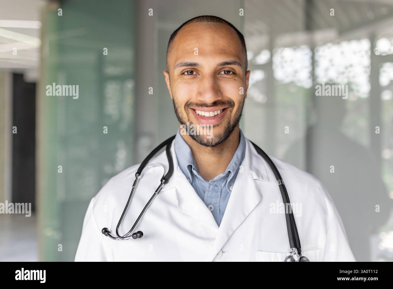 Zufriedener erfolgreicher Arzt in Nahaufnahme lächelnd und in die Kamera schauend. Arzt in weißem medizinischem Mantel und mit Stethoskop im Büro am Arbeitsplatz, moderne Klinik. Stockfoto