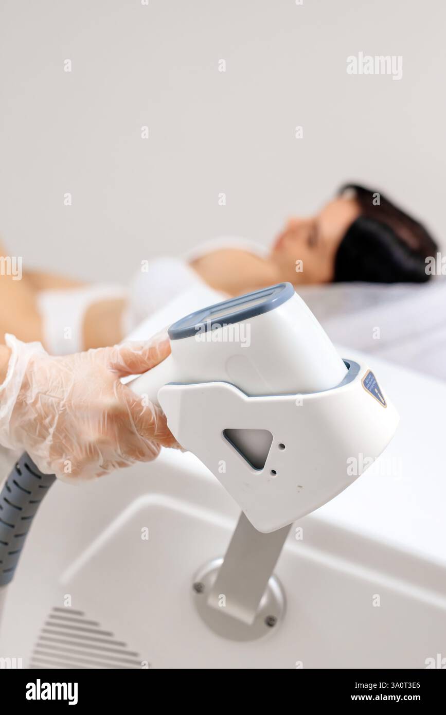 Ein Dermatologe steht mit Geräten zur Haarentfernung. Der Kosmetiker passt die Geräteeinstellungen für die Haarentfernung mit dem Laser an Stockfoto Ein Dermatologe steht mit Geräten zur Haarentfernung. Der Kosmetiker passt die Geräteeinstellungen für die Haarentfernung mit dem Laser an Stockfoto