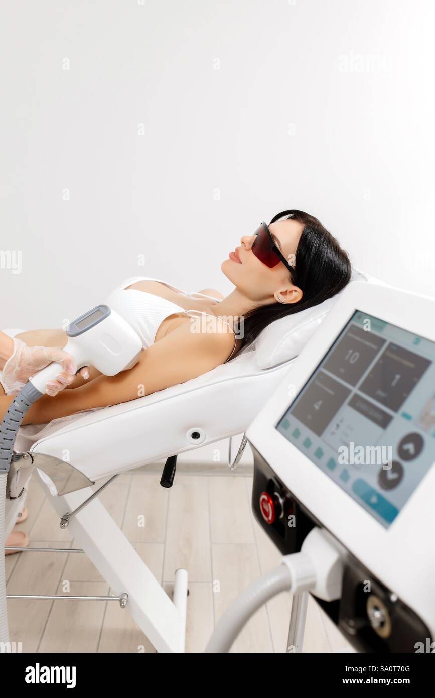 Körperhygiene. Laserhaarentfernung des Körpers. Ein Kosmetiker entfernt Körperhaare junger Frauen. Laserhaarentfernung in einer Kosmetikklinik. Stockfoto Körperhygiene. Laserhaarentfernung des Körpers. Ein Kosmetiker entfernt Körperhaare junger Frauen. Laserhaarentfernung in einer Kosmetikklinik. Stockfoto