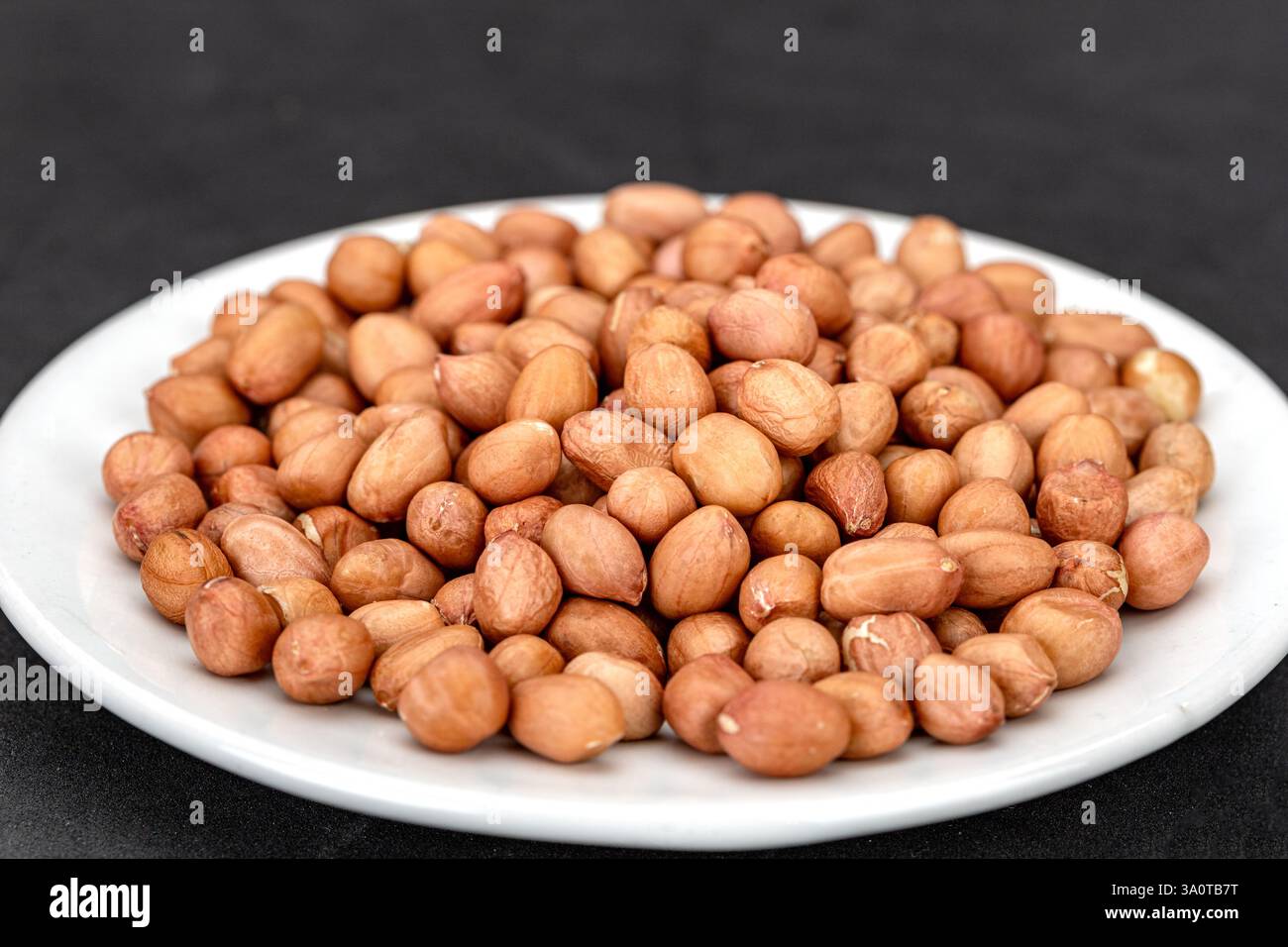 Eine Menge rohe Erdnüsse auf einem weißen Teller, bereit zum Kochen. Stockfoto