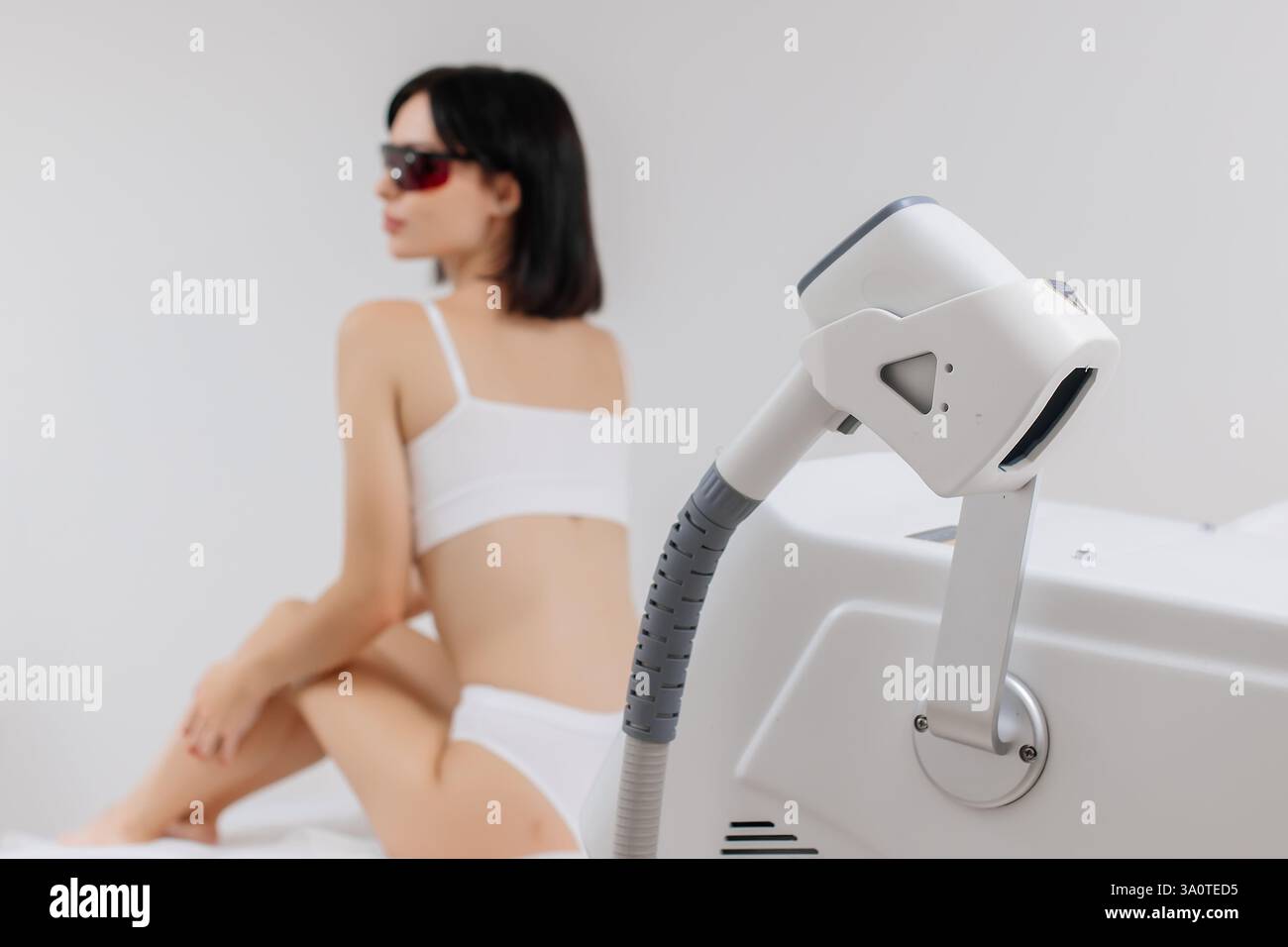 Ein Dermatologe steht mit Geräten zur Haarentfernung. Der Kosmetiker passt die Geräteeinstellungen für die Haarentfernung mit dem Laser an Stockfoto Ein Dermatologe steht mit Geräten zur Haarentfernung. Der Kosmetiker passt die Geräteeinstellungen für die Haarentfernung mit dem Laser an Stockfoto